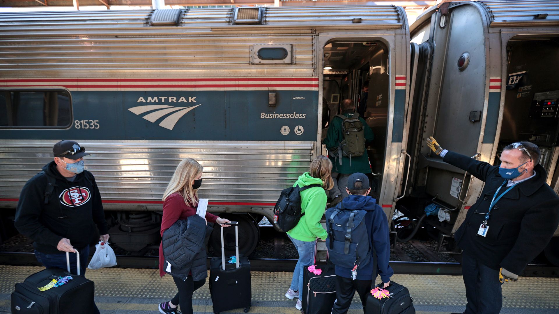 Passengers board a train while pulling suitcases. 