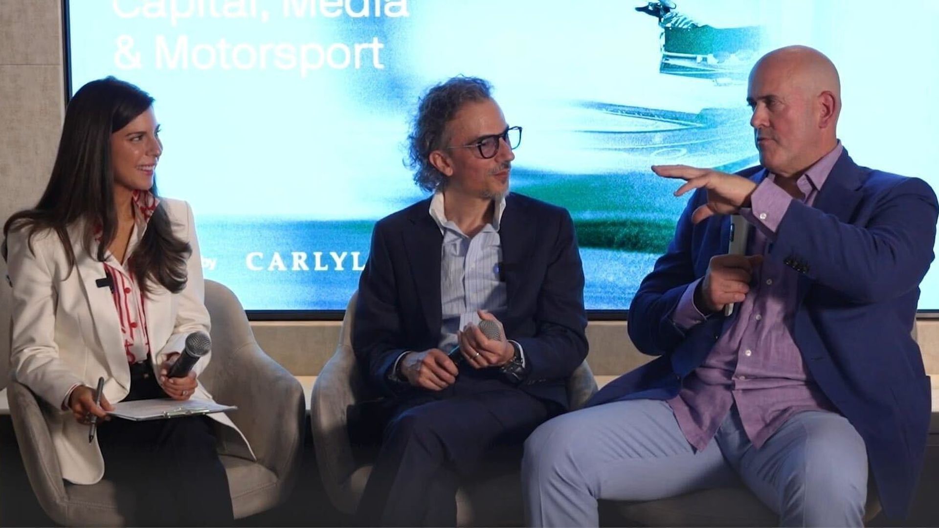 Axios' Sara Fischer, Laurent Mekies, team principal of Oracle Red Bull Racing, and Carlyle CEO Harvey Schwartz sit on a stage before a blue screen displaying "Inside the Monaco Circuit: Capital, Media & Motorsport."