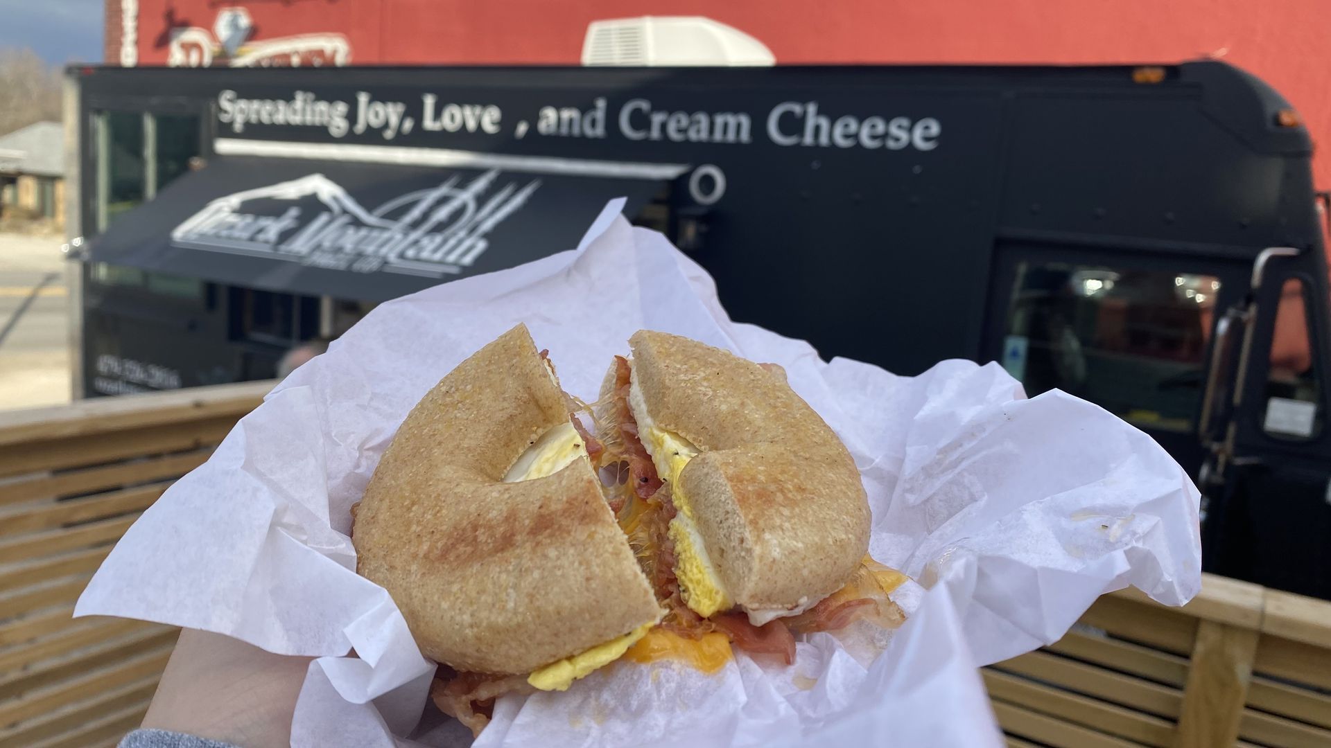A bagel breakfast sandwich held up in front of a food truck