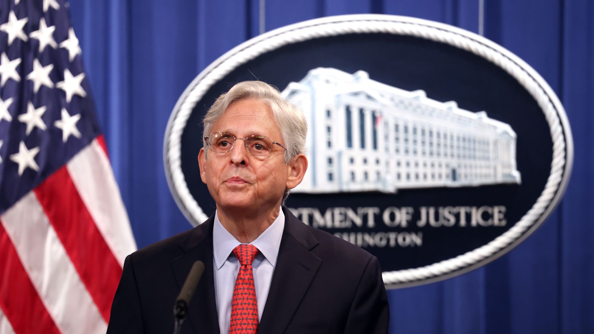 A man stands at a podium next to an American flag and in front of a large Department of Justice seal.