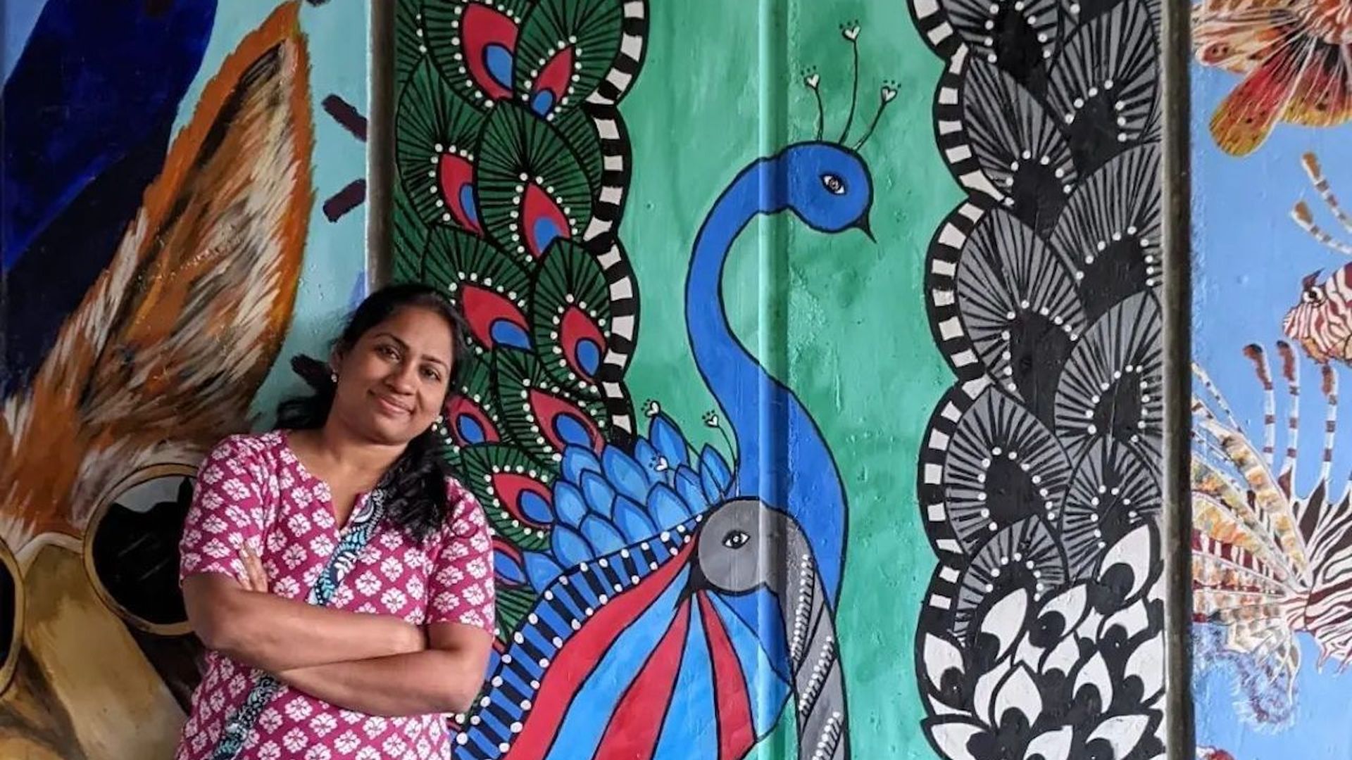 A woman stands next to a mural.