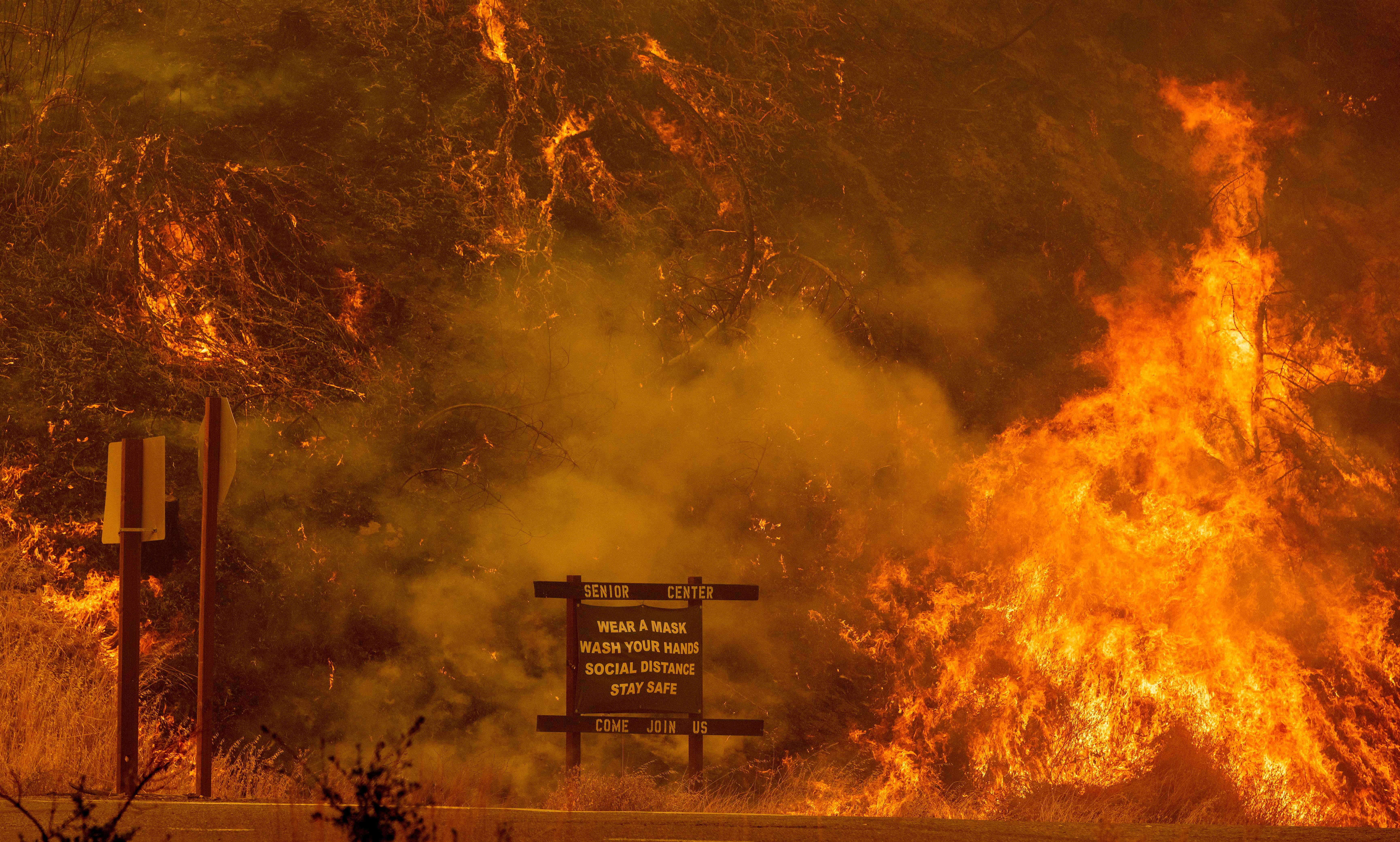 A sign warning people about Covid-19 is surrounded by flames during the Hennessey fire near Lake Berryessa in Napa, California on August 18