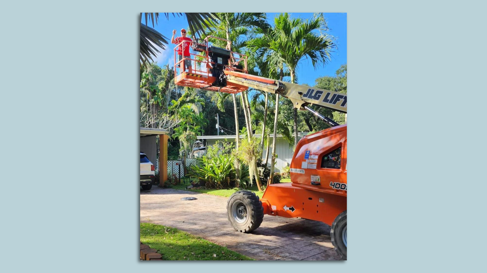 A man in a boom lift puts holiday lights on his tree.