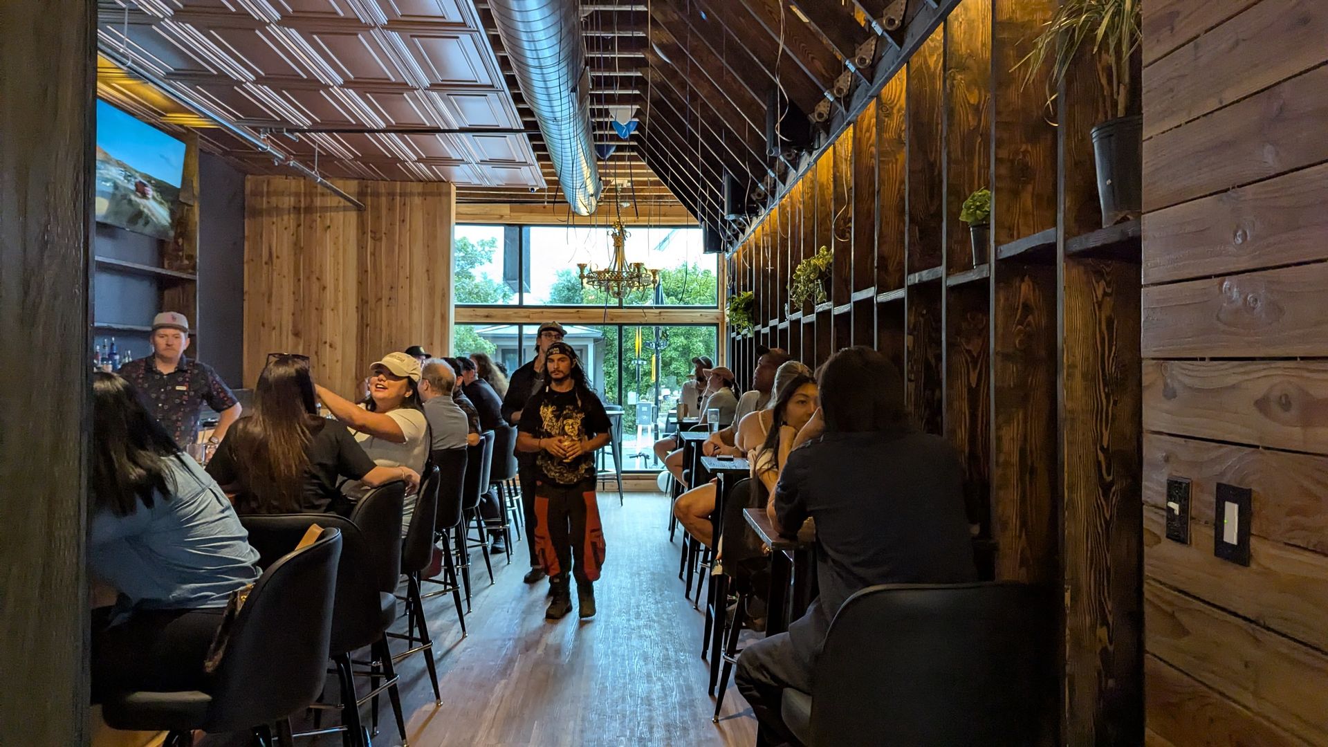 People at a bar with wood walls and a chandelier.