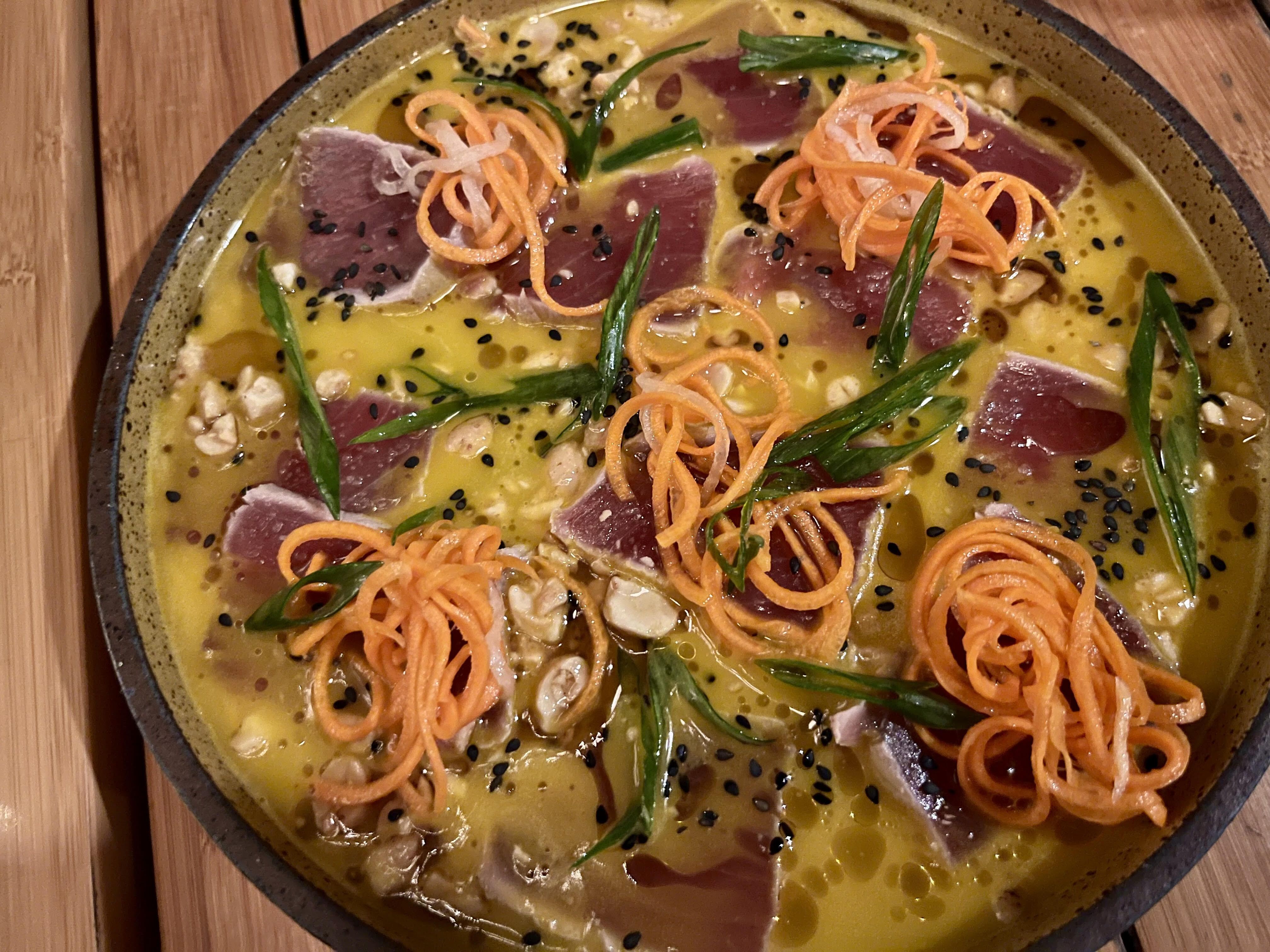 A circular dish made with raw fish and a yellow sauce.