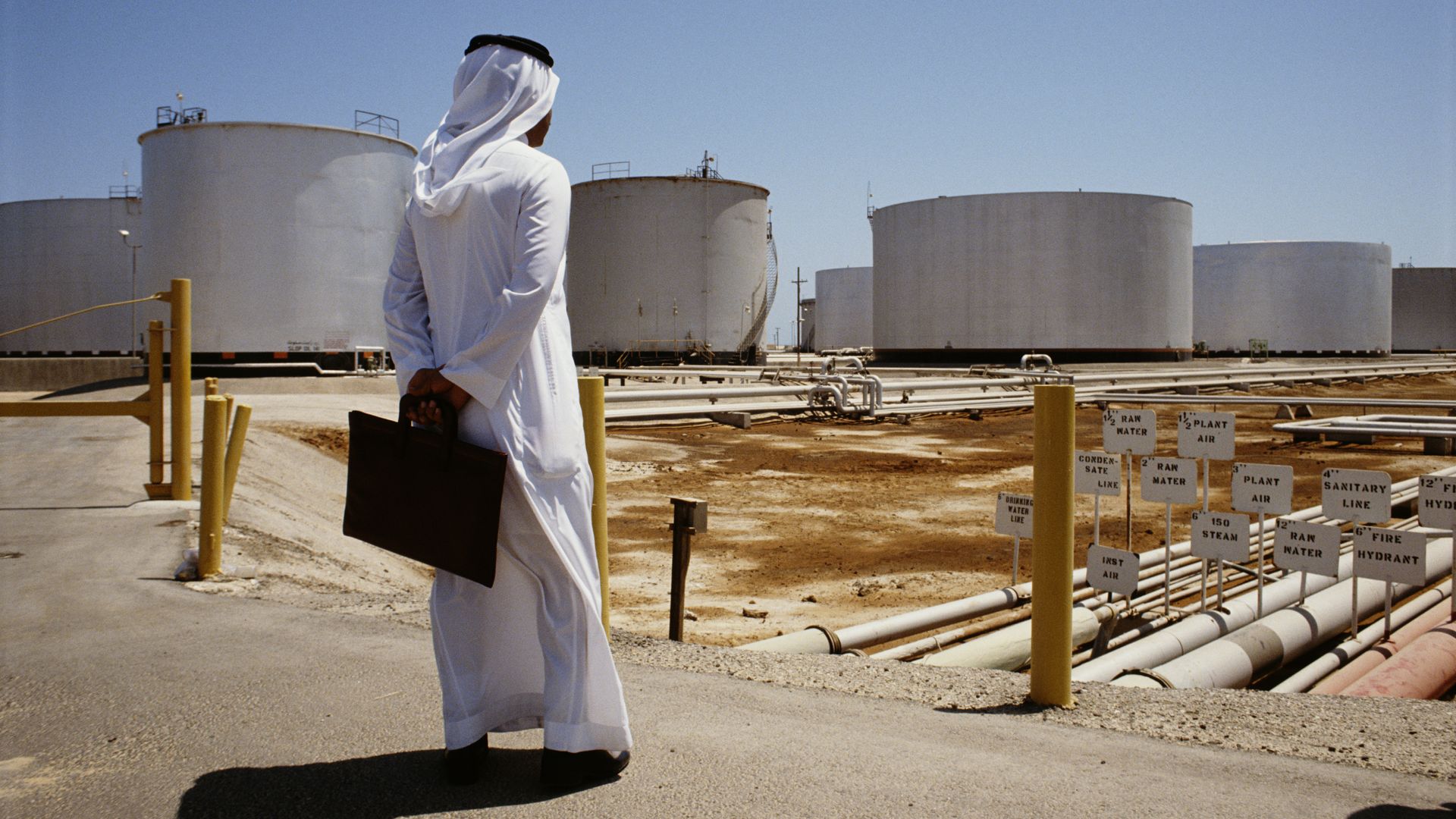 Photo of a Saudi man standing with a briefcase gazing at some Aramco refineries.