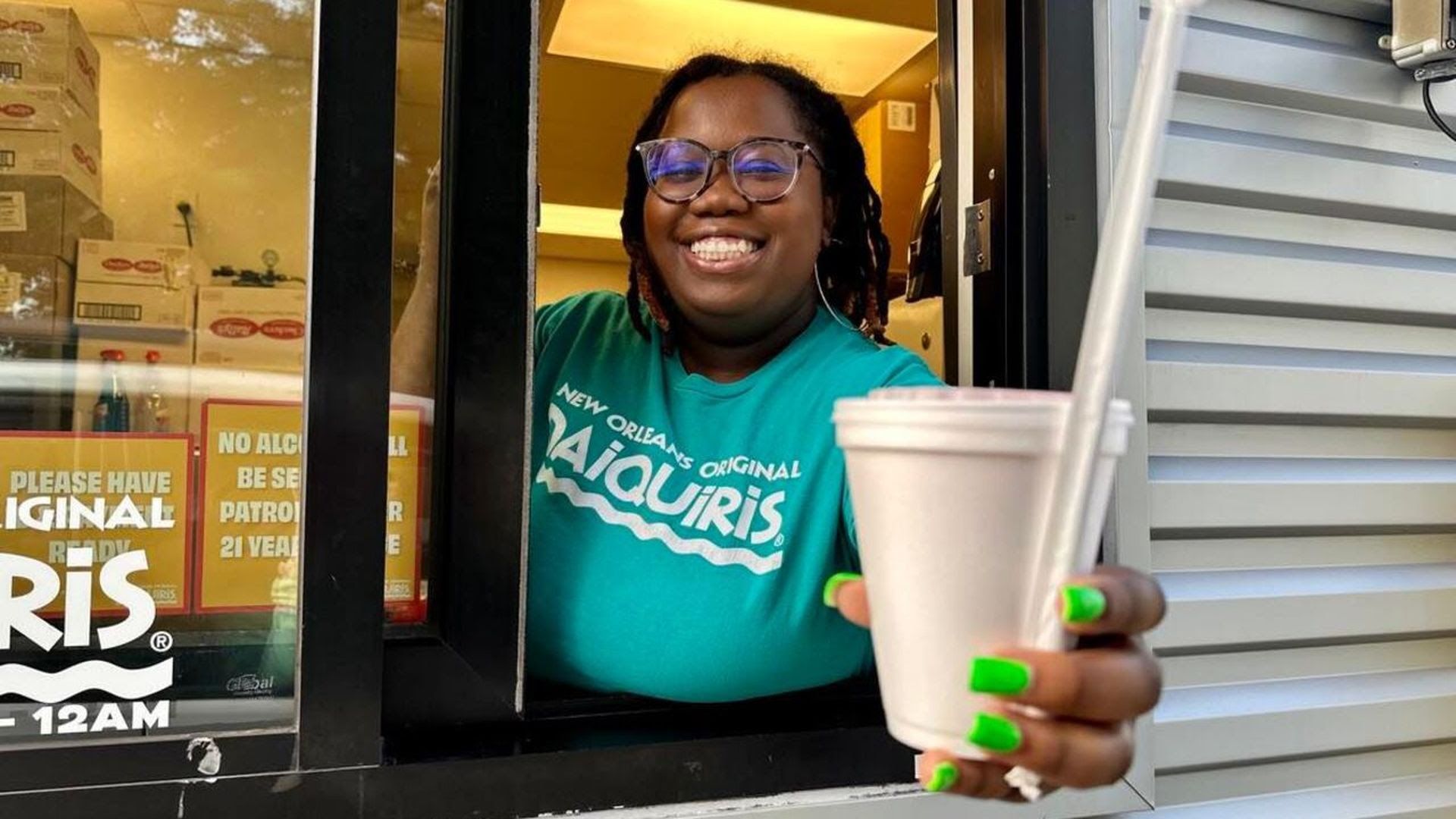A woman smiles as she passes a Styrofoam cup with a straw out of a drive-thru window.