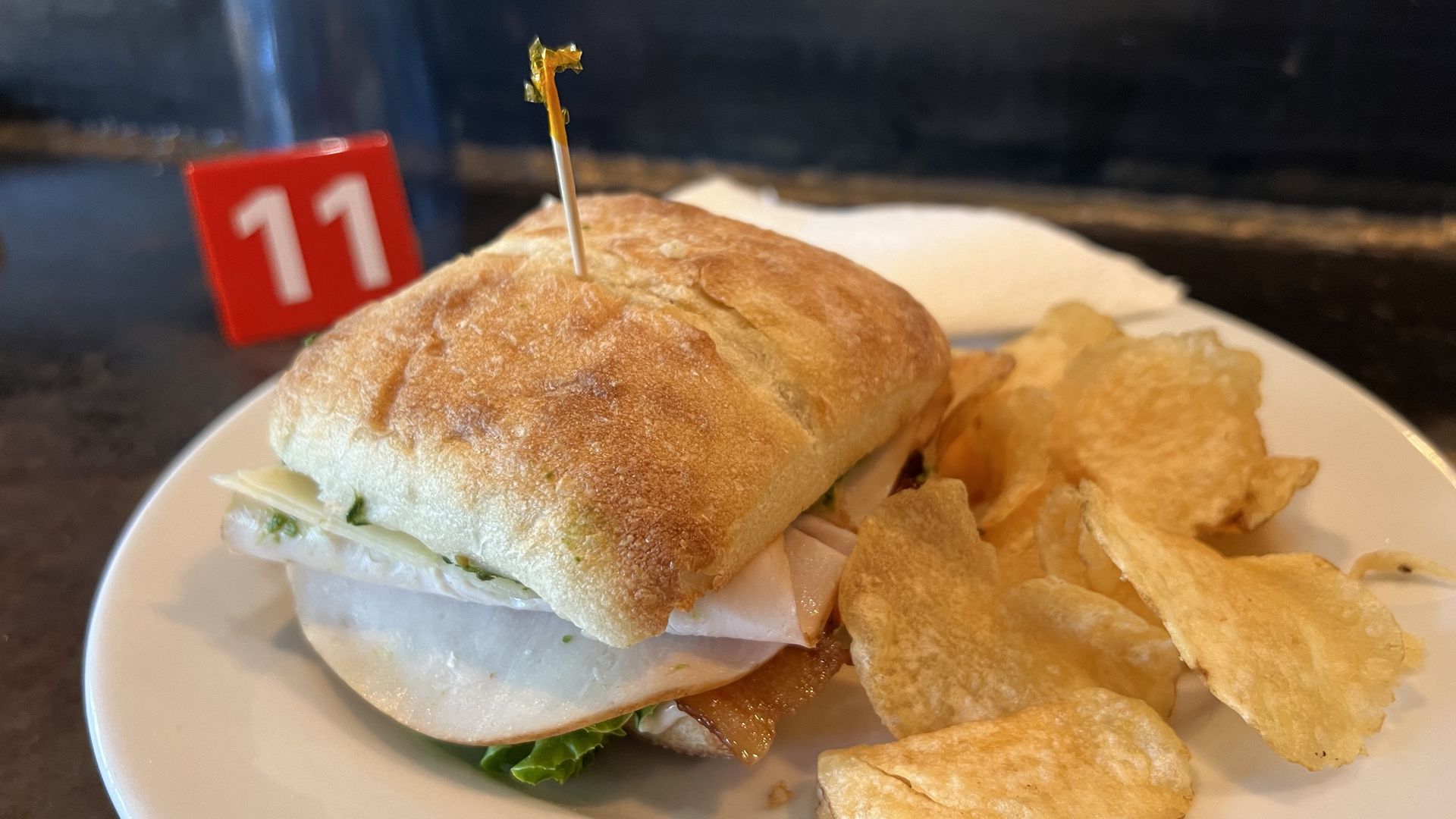 A sandwich with a toothpick through its center and a plate of potato chips