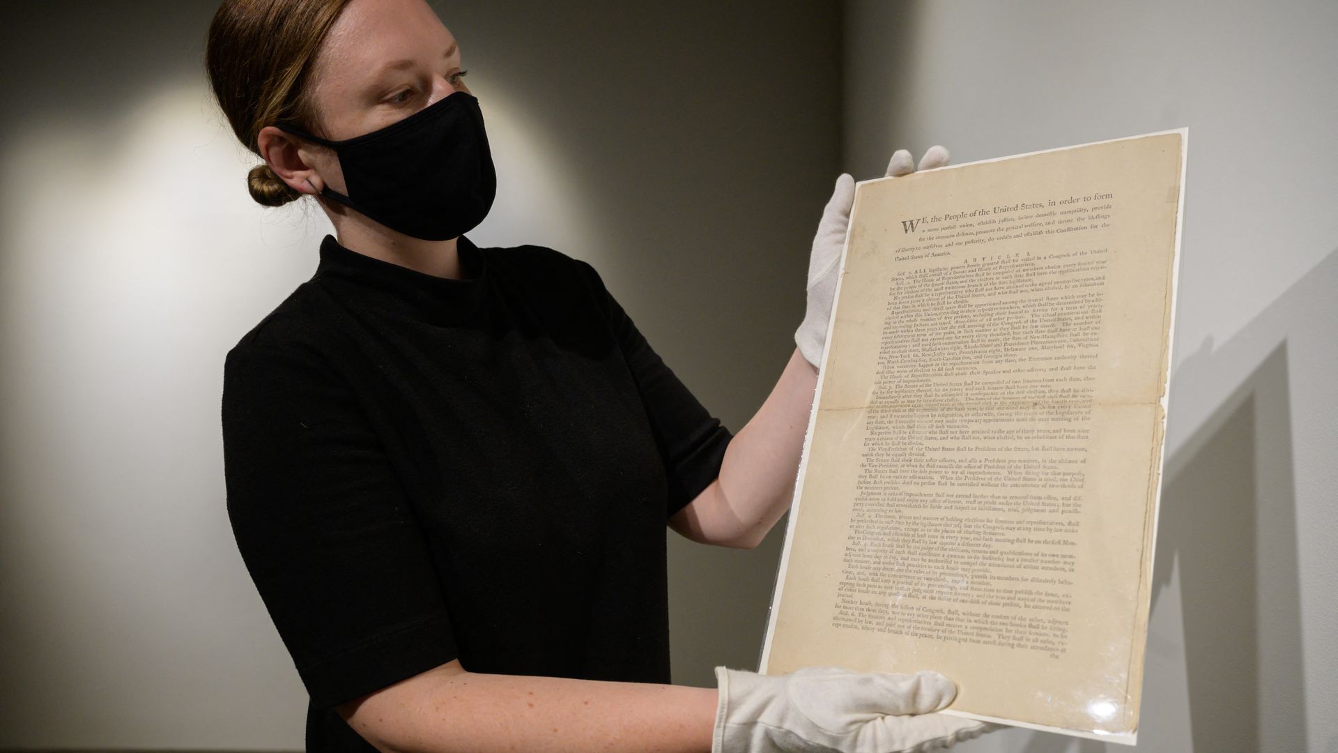 Photo of masked person holding a framed page of the U.S. constitution