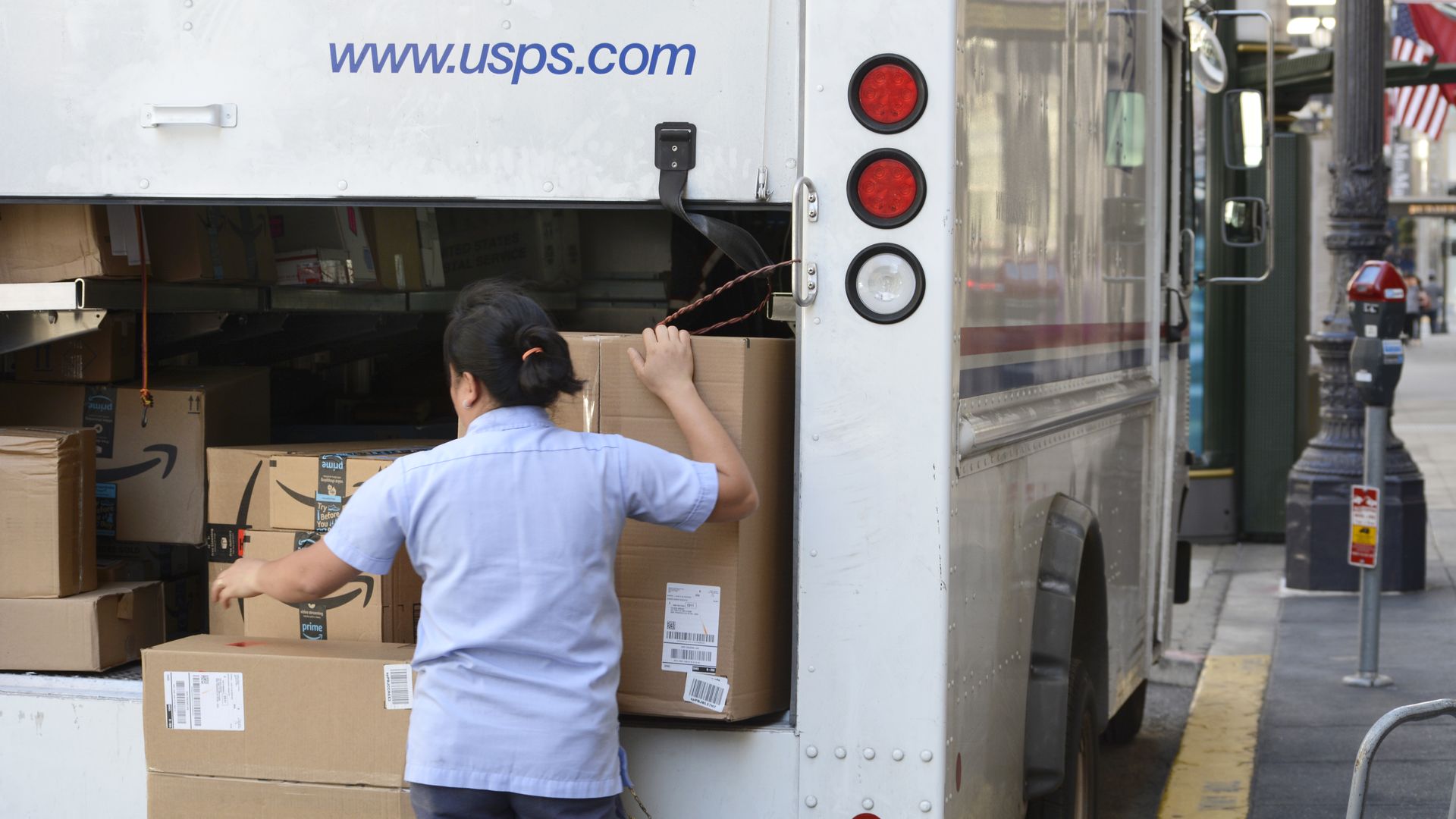 USPS worker loads up Amazon packages in truck.