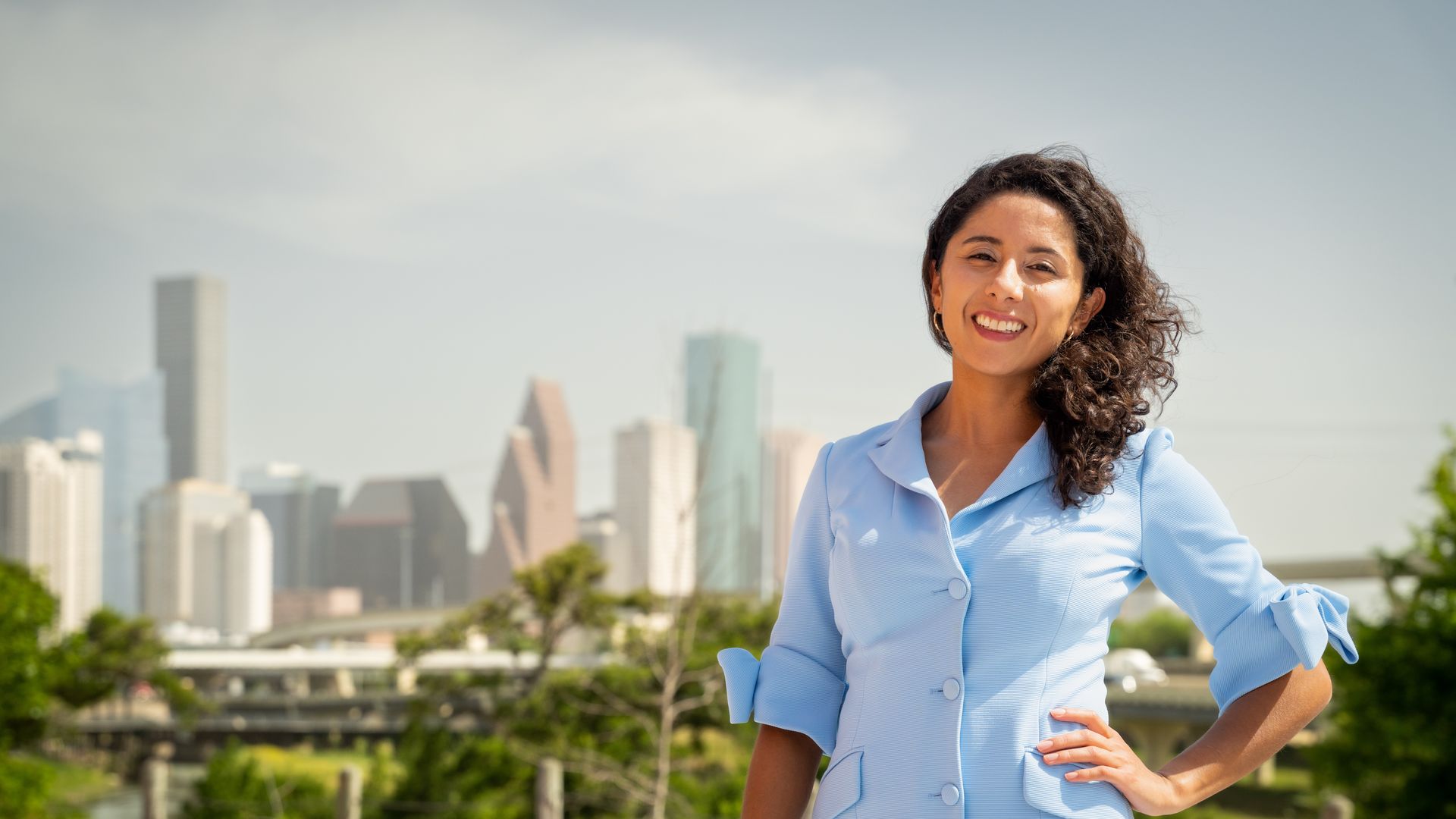 Harris County Judge Lina Hidaglo, in blue, smiles with the Houston skyline in the background