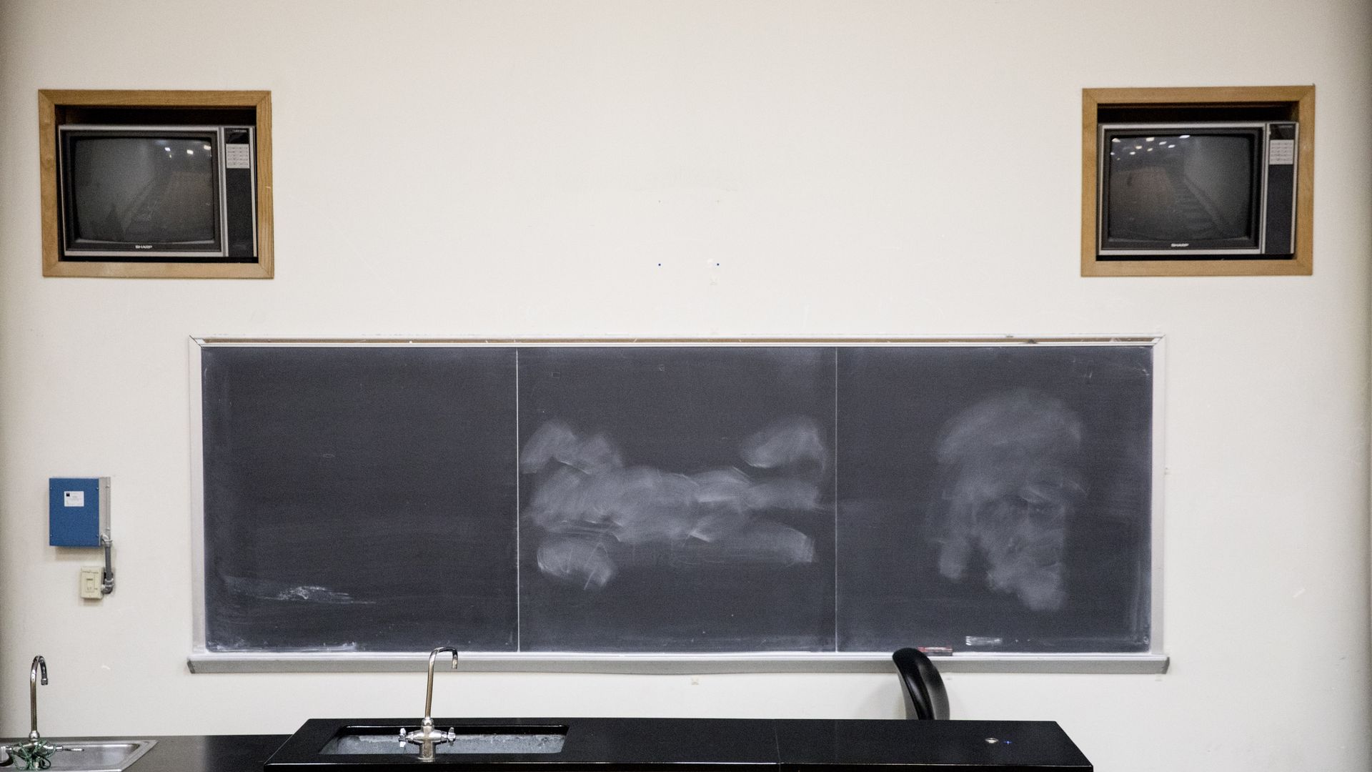 Two vintage television sets sit above a chalkboard inside a classroom.