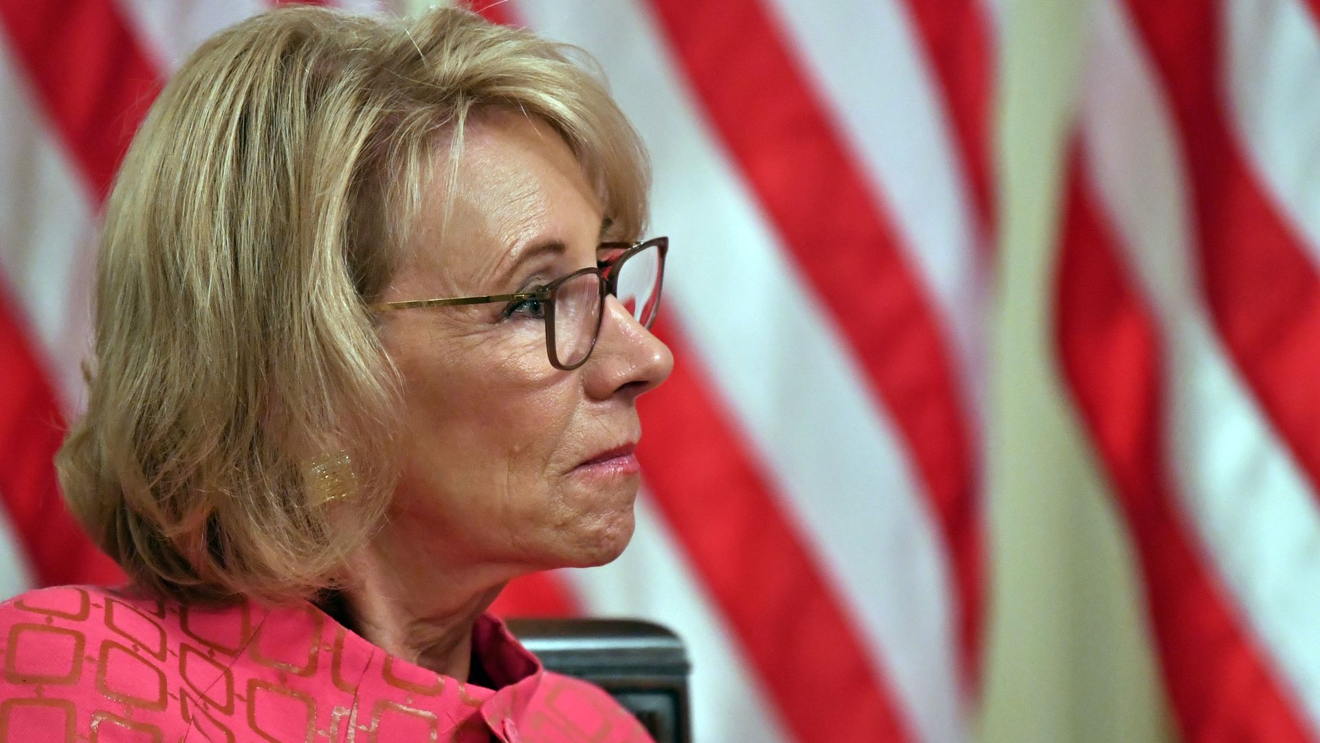 Photo of Betsy DeVos' side profile against the backdrop of an American flag