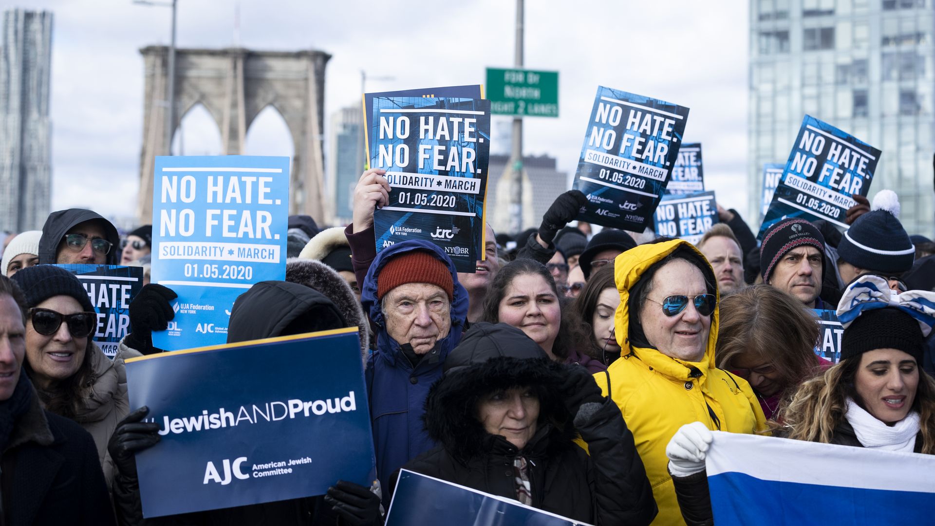 Marchers hold signs that reads "No Hate No Fear" and "Jewish and Proud" as they walk across the Brooklyn Bridge