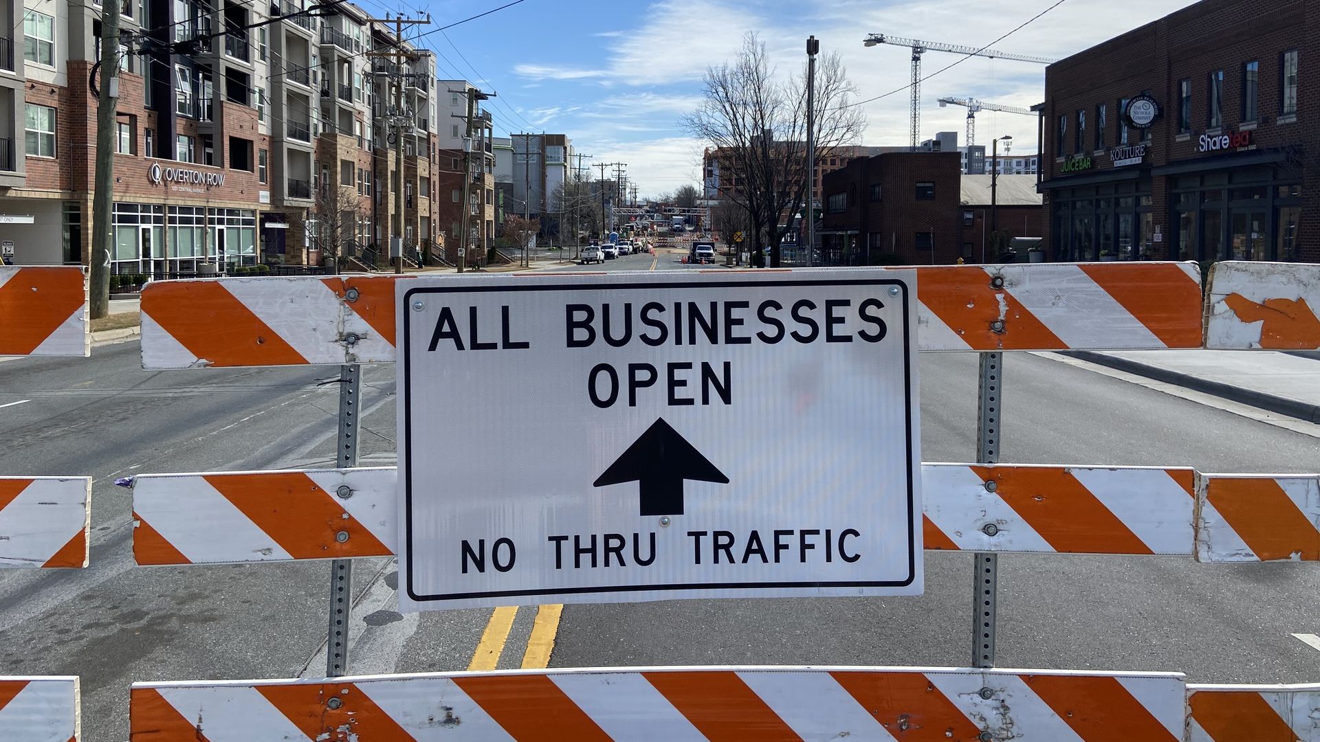 A barrier blocking off the road in front of the street with a sign that reads "All businesses open, no thru traffic"