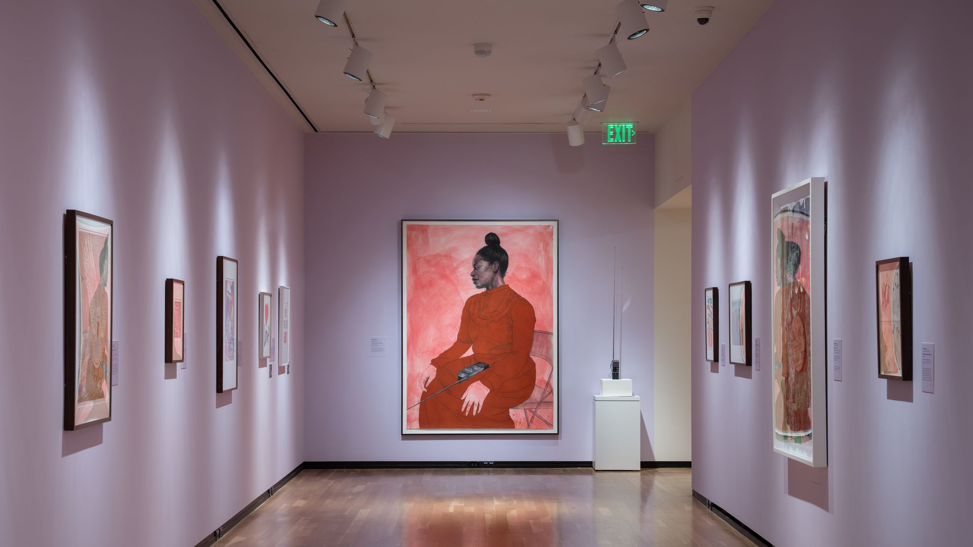 Lavender-walled museum hallway with track lighting and framed artworks along both sides; at the far end sits a large pink portrait of a seated woman in an orange-red dress, with a green EXIT sign overhead.