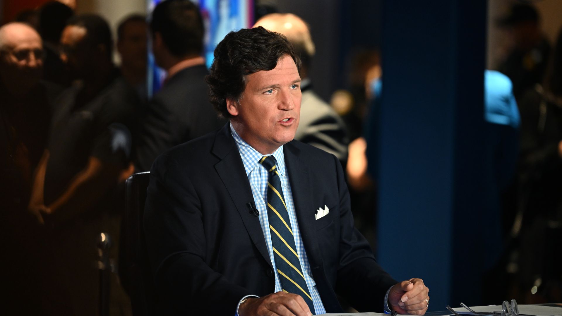 Photo of Tucker Carlson sitting at a desk while he hosts Fox and Friends