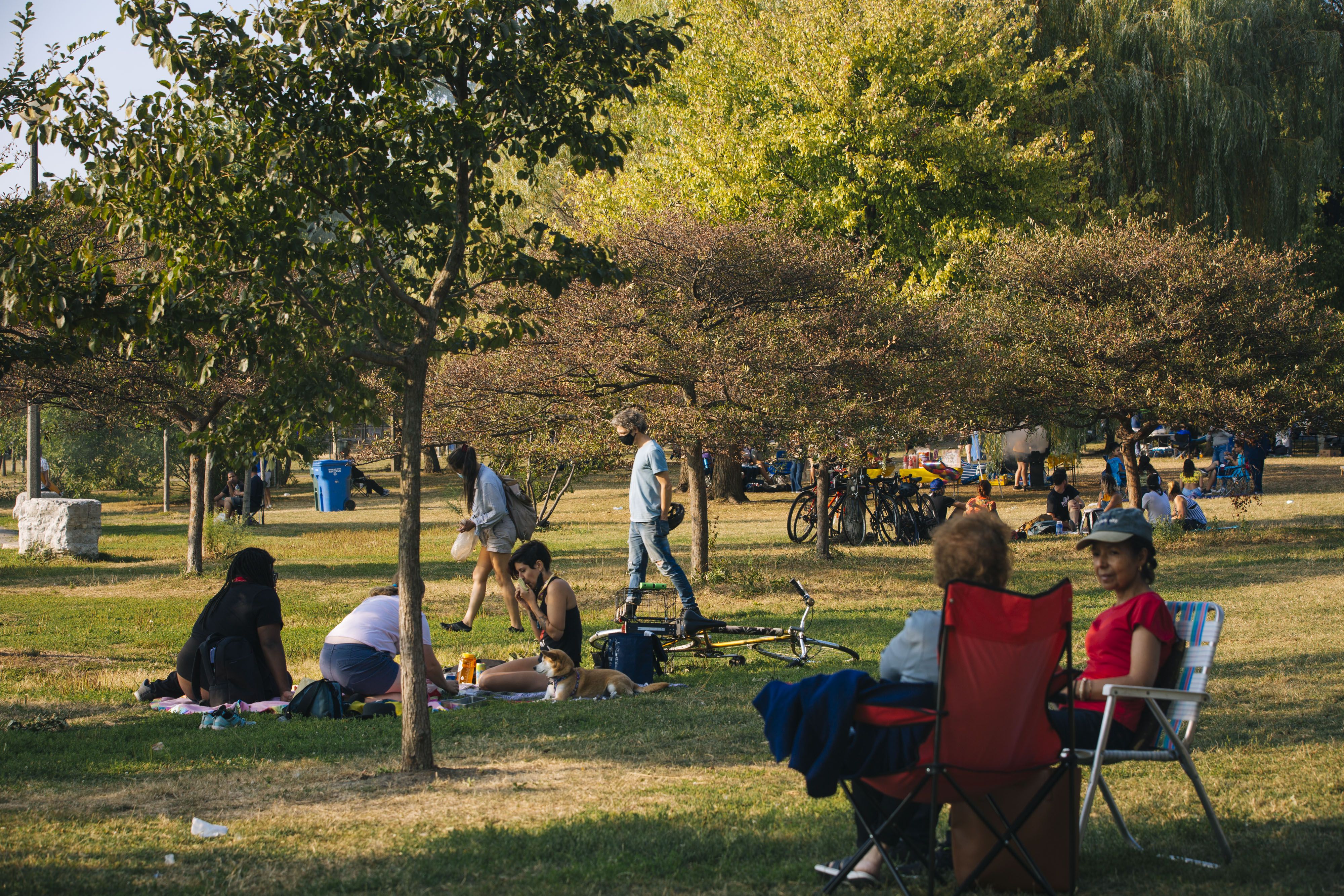 People gather in Humboldt Park, having picnics and sitting in lawn chairs chatting.