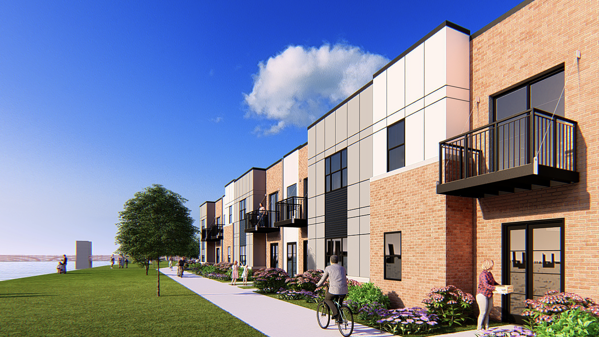 Modern mixed brick and panel townhouses with black balconies along a waterfront sidewalk with grass, trees, and people walking and biking under a bright blue sky.