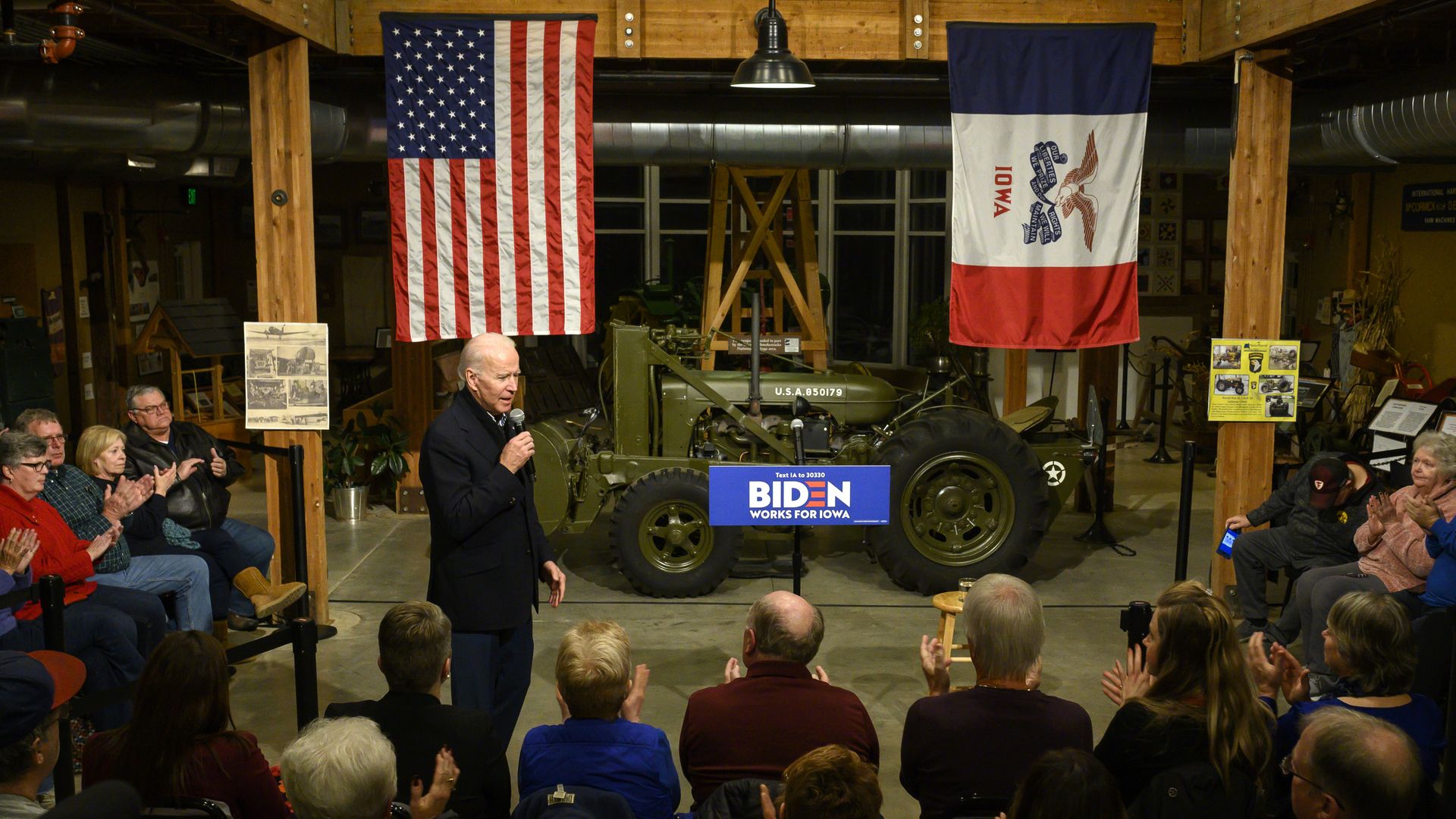 Biden addresses a crowd on a stage with an American flag and Iowa flag in the background