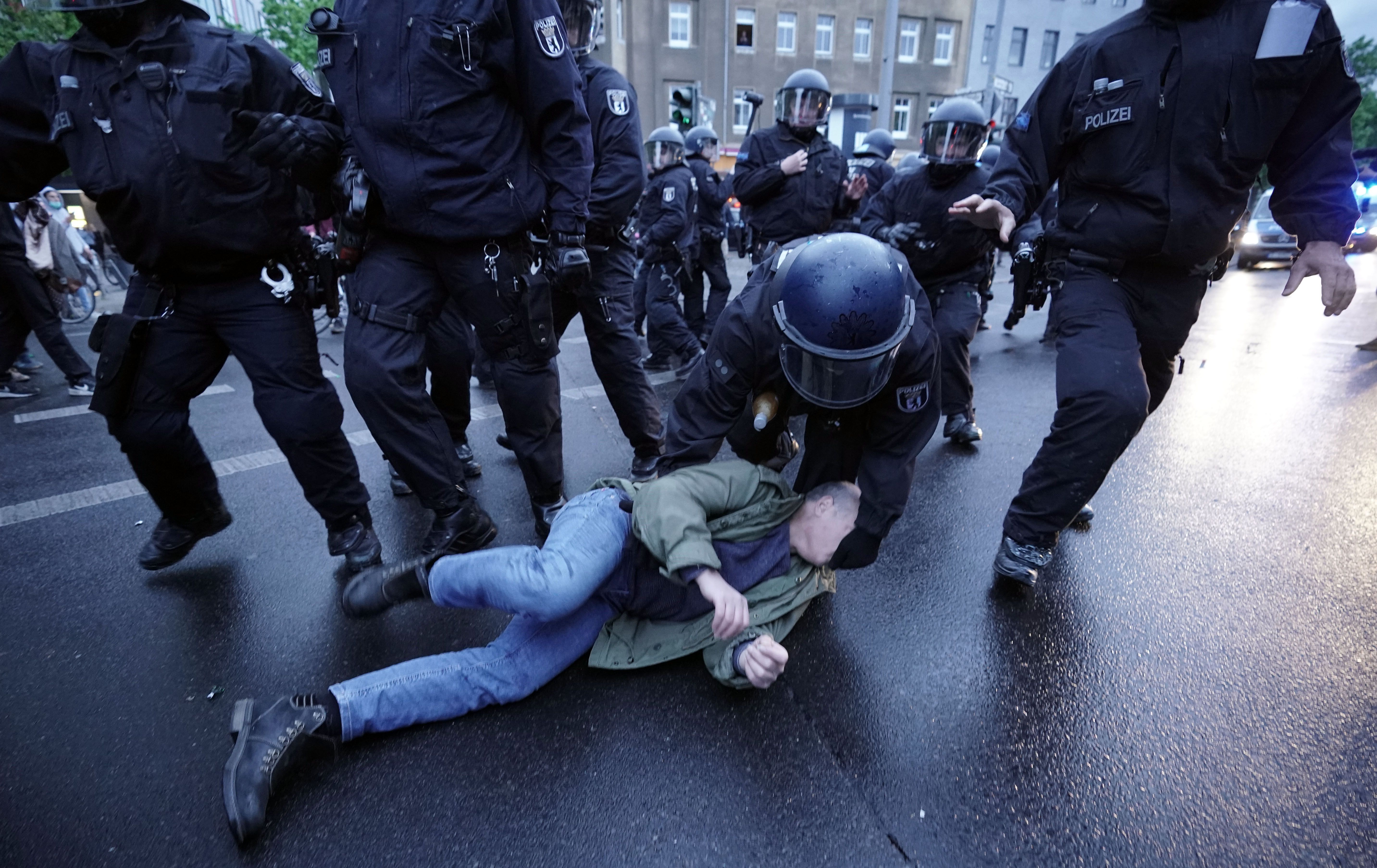 In this image, police strike a man laying on the ground