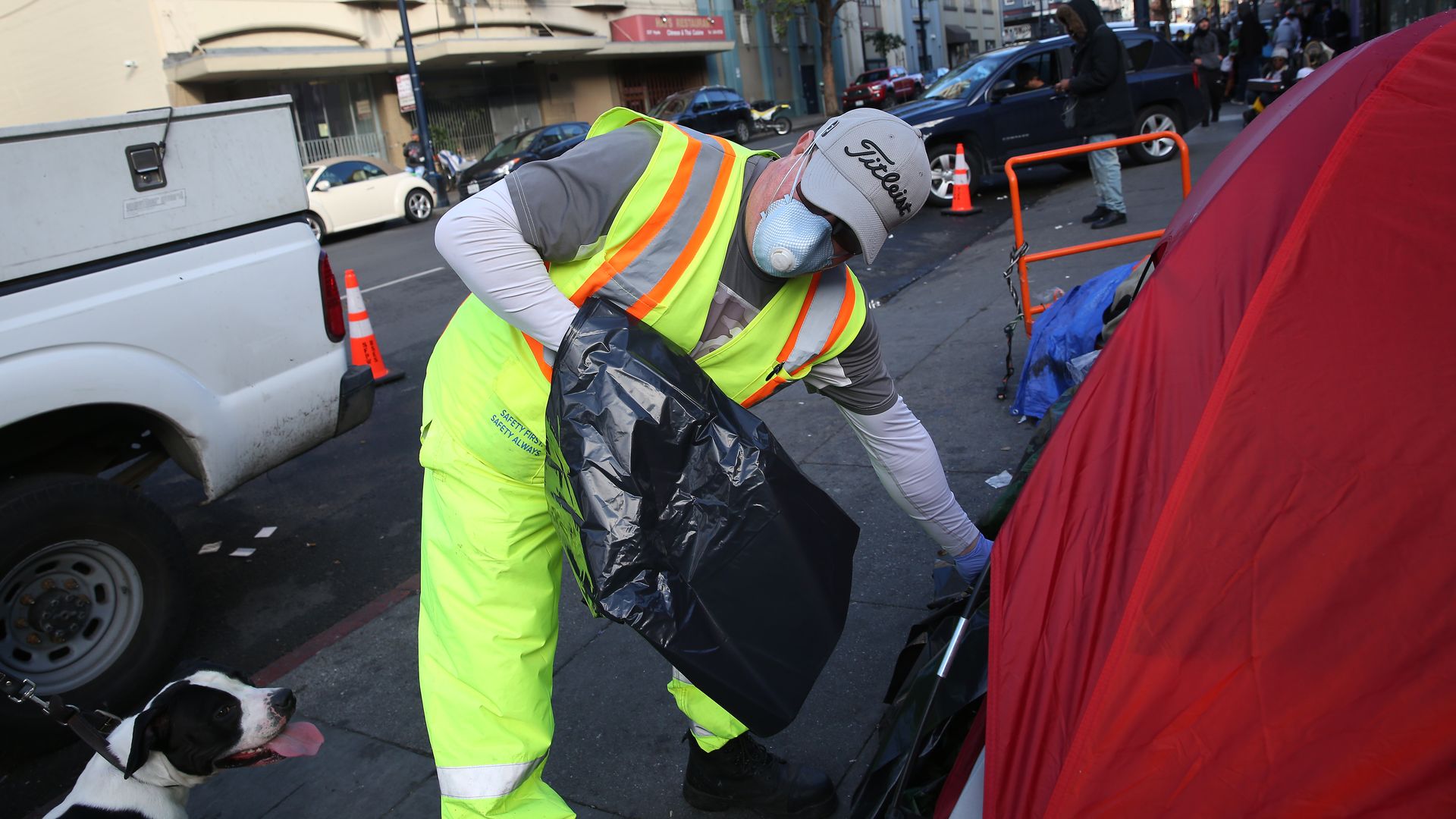 John Duport, Department of Public Works worker, hands a trash bag to someone in a tent on Hyde Street while cleaning the street and sidewalk on Wednesday, March 25, 2020 in San Francisco, Calif.