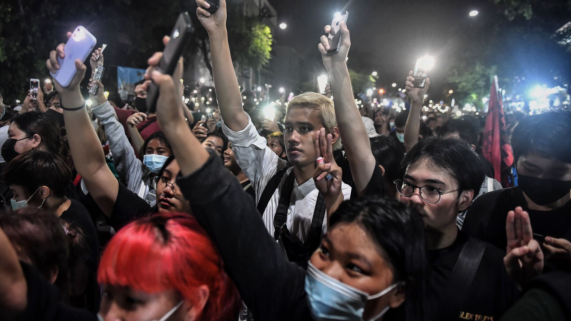 Pro-democracy protesters give the three-finger salute as they hold up their mobile phones with lights while gathering outside the Government House in an anti-government rally in Bangkok on October 14