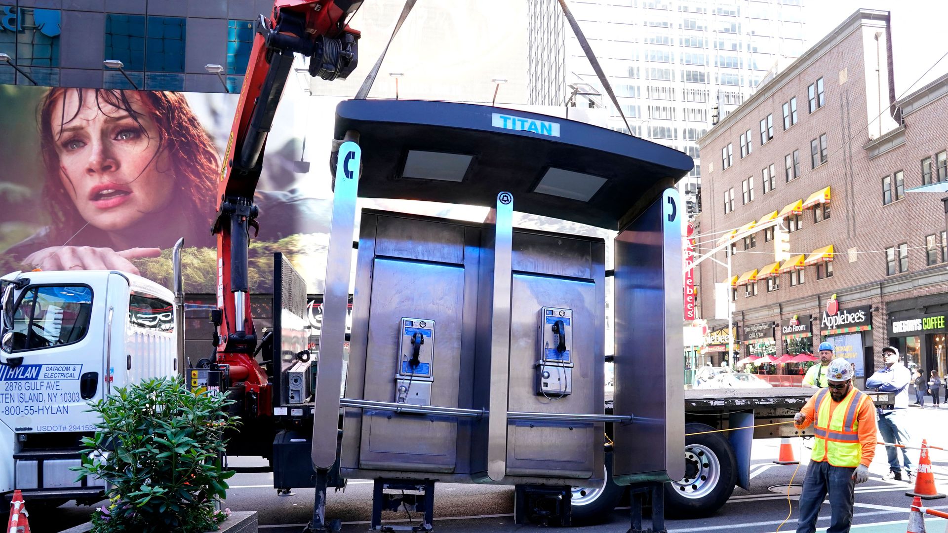 A crane removes a block of two payphones from a sidewalk in New York City