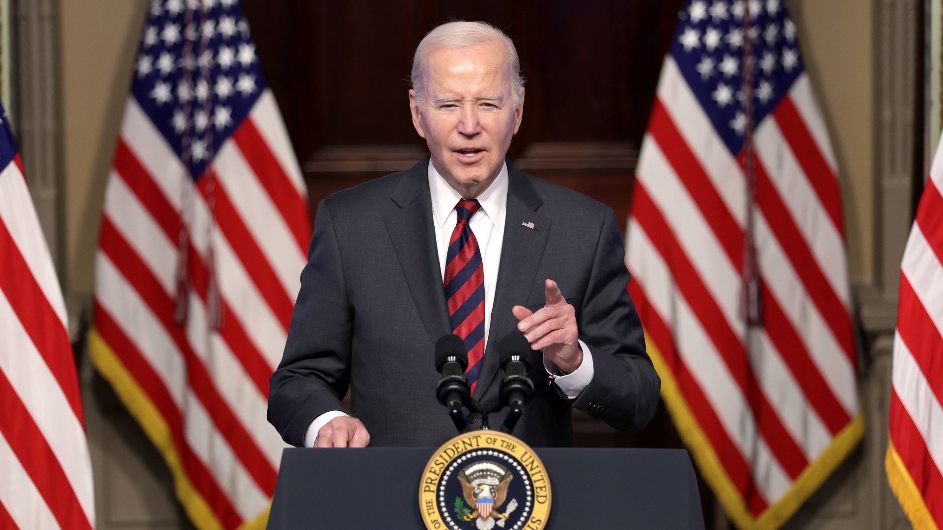 Biden speaks at a lectern with American flags behind him.