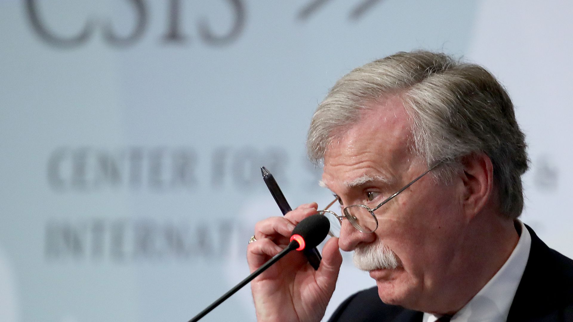 John bolton adjusting his glasses at a podium