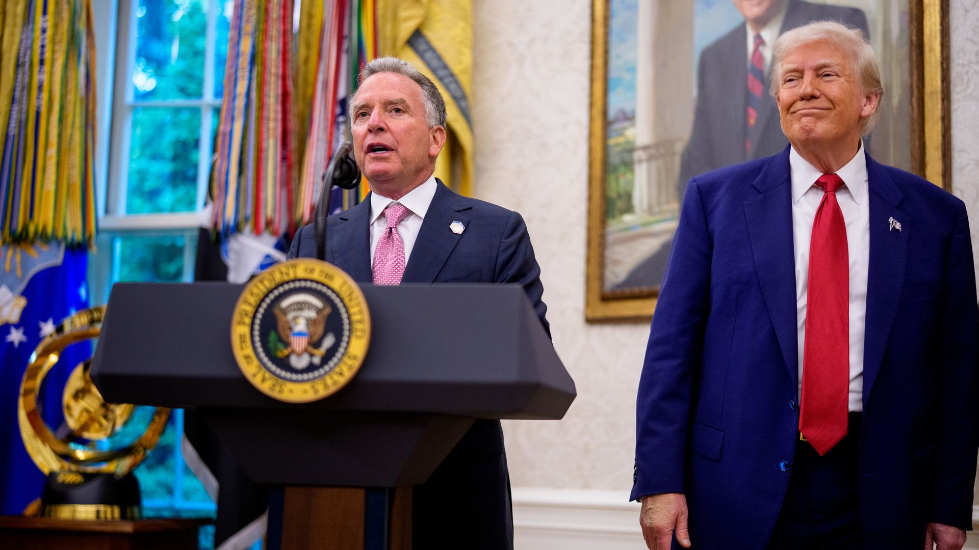 Man at podium next to man in red tie
