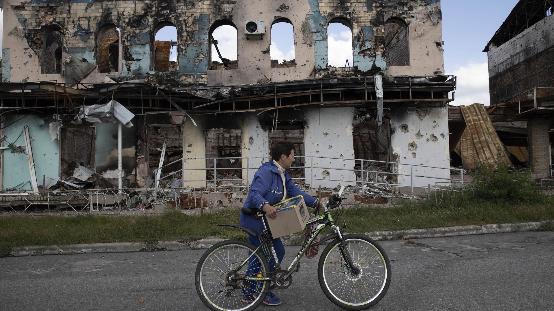 A Ukrainian woman is seen with a bicycle in front of a demolished building in Izium, Kharkiv Oblast, Ukraine on September 18