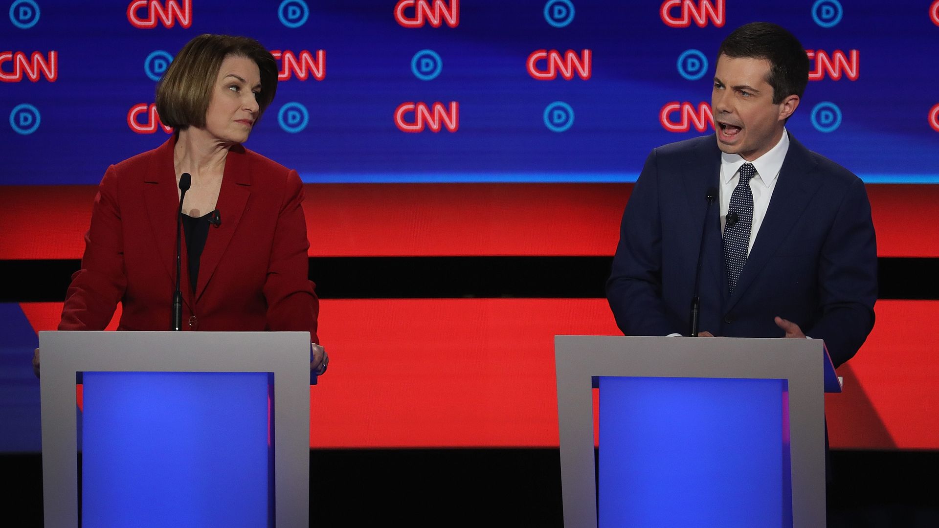 In this image, Klobuchar and Pete Buttigieg speak behind two different podiums on stage with the CNN logo behind them.
