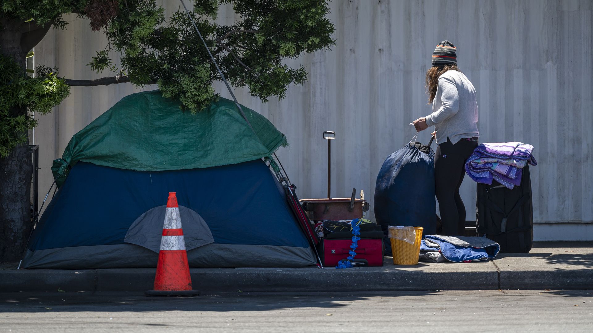 Photo of an unhoused person collecting belongings next to a tent on a sidewalk