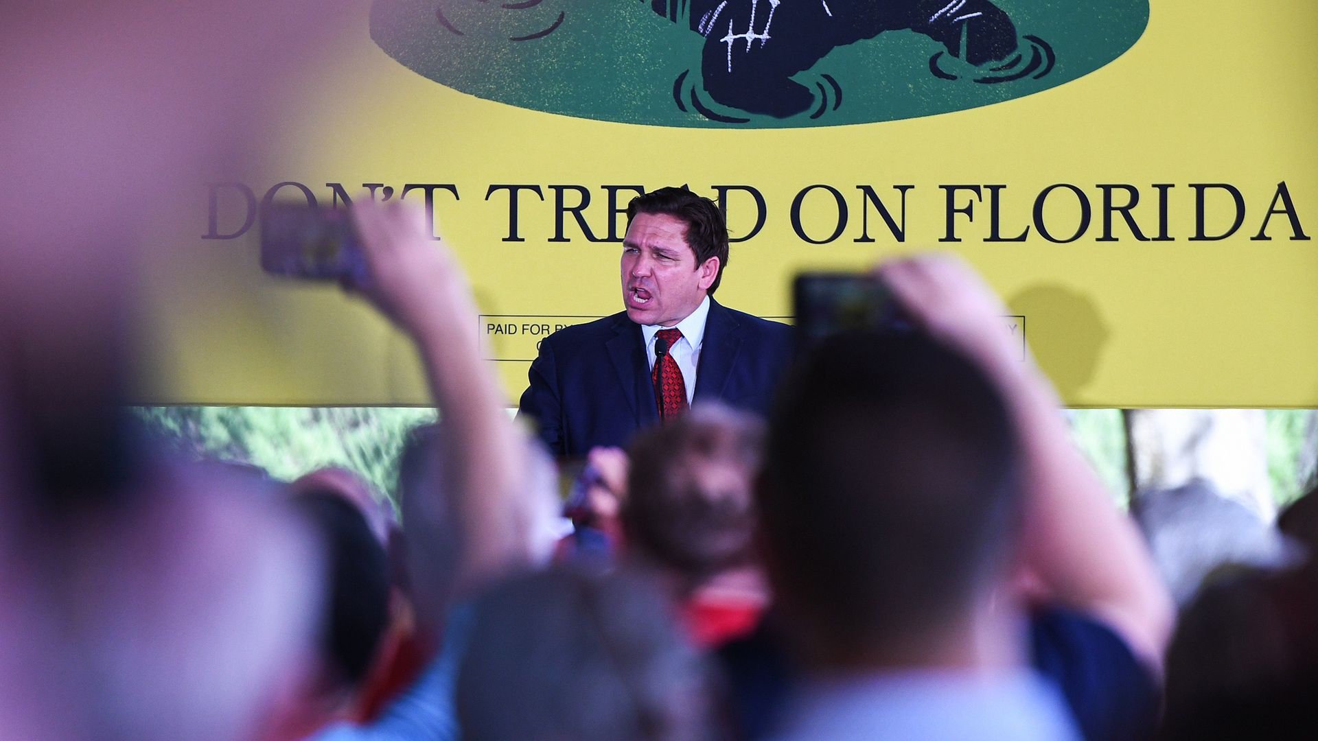 Photo of Ron DeSantis speaking from a podium at a rally against the backdrop of a banner that says "Don't Tread On Florida"