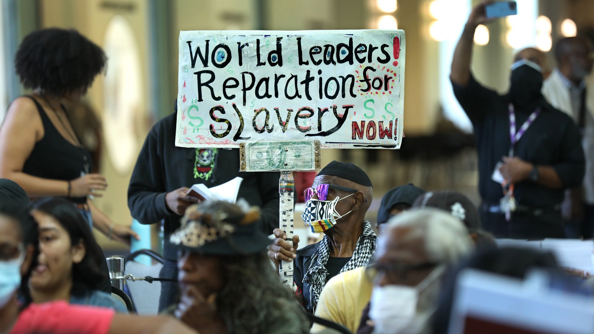 person holds up sign that says "world leaders! reparations for slavery now!"