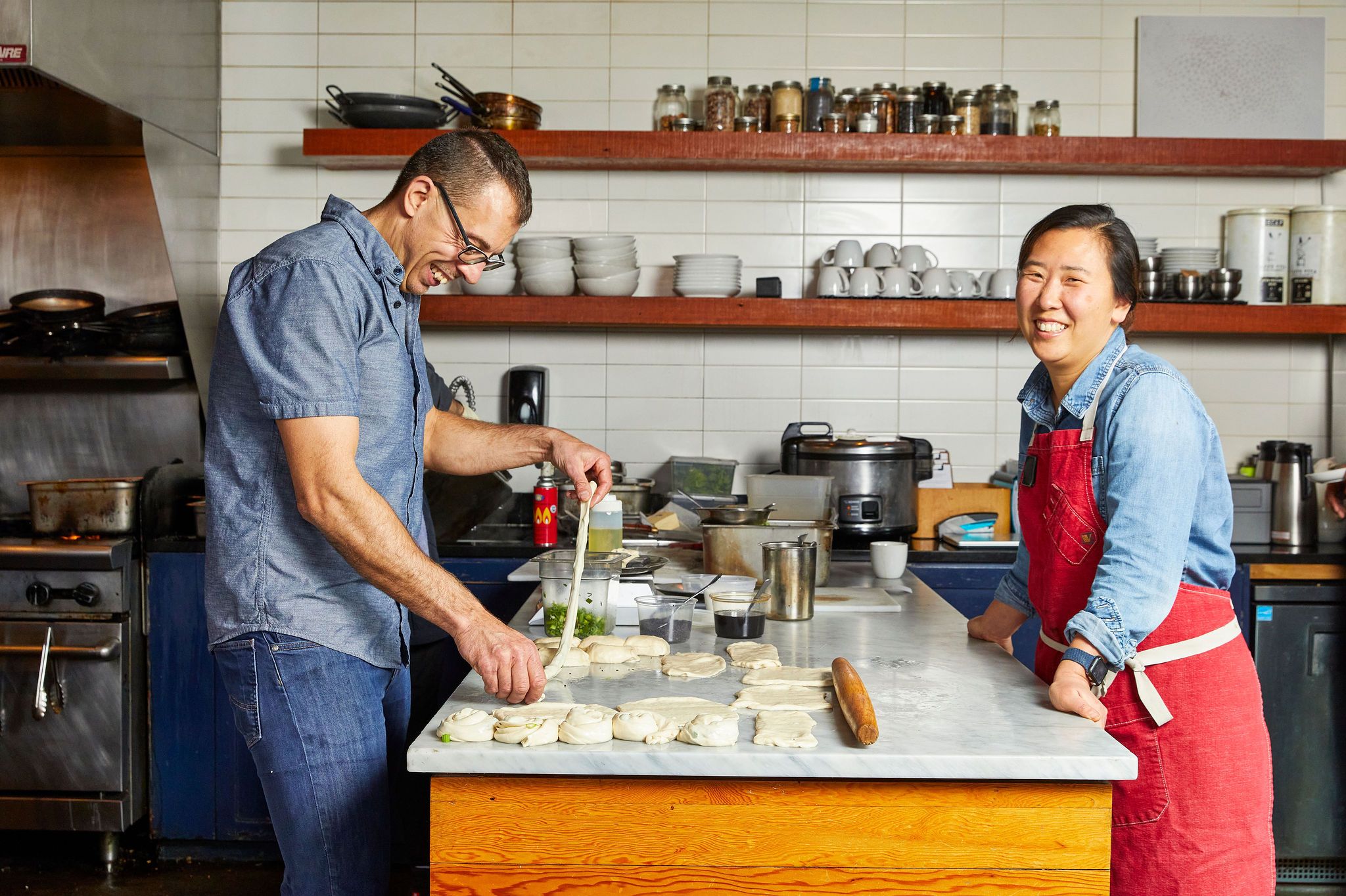 Two people standing on opposite ends of a countertop in a kitchen of a restaurant, both smiling. 