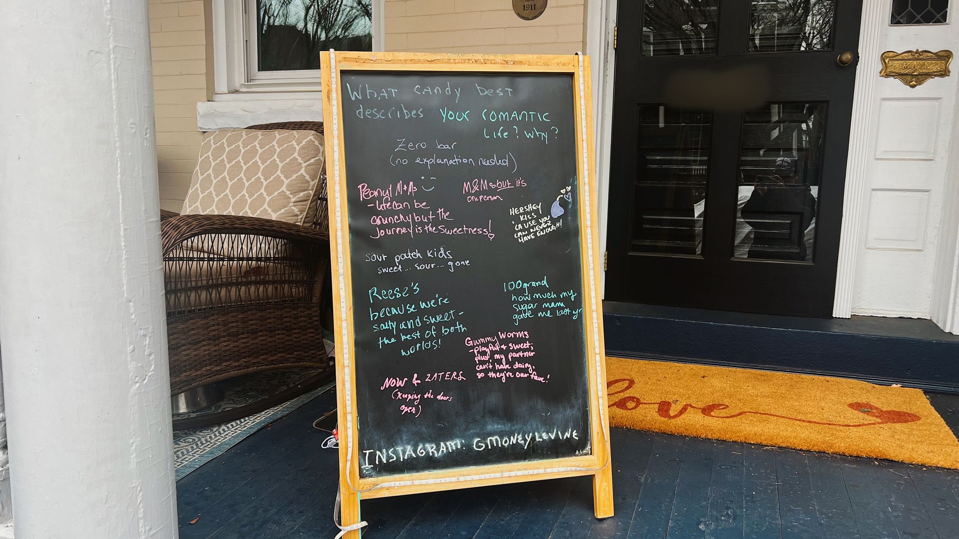 a wooden-framed chalkboard with the question "what candy best described your romantic life? why?" on the porch of a house. It's filled with a bunch of responses in different colors.