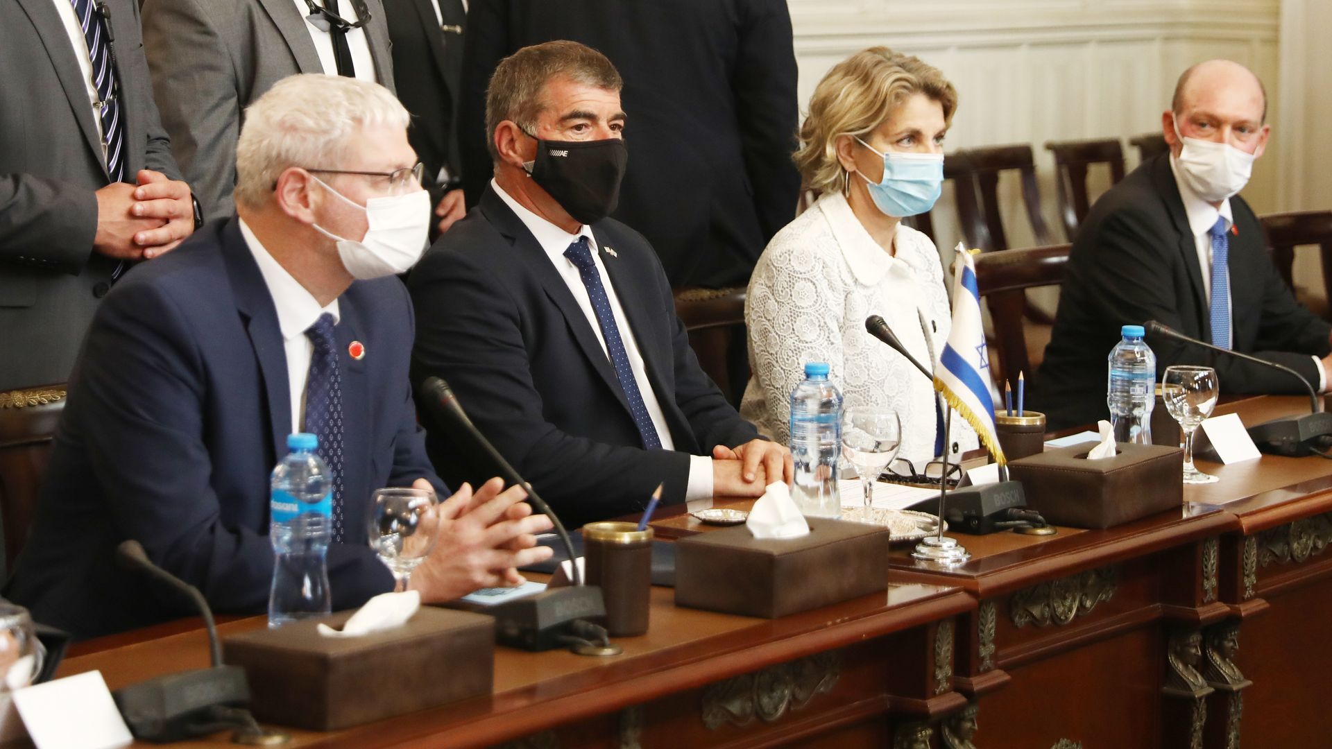 Two men and one woman sit at a table while wearing masks