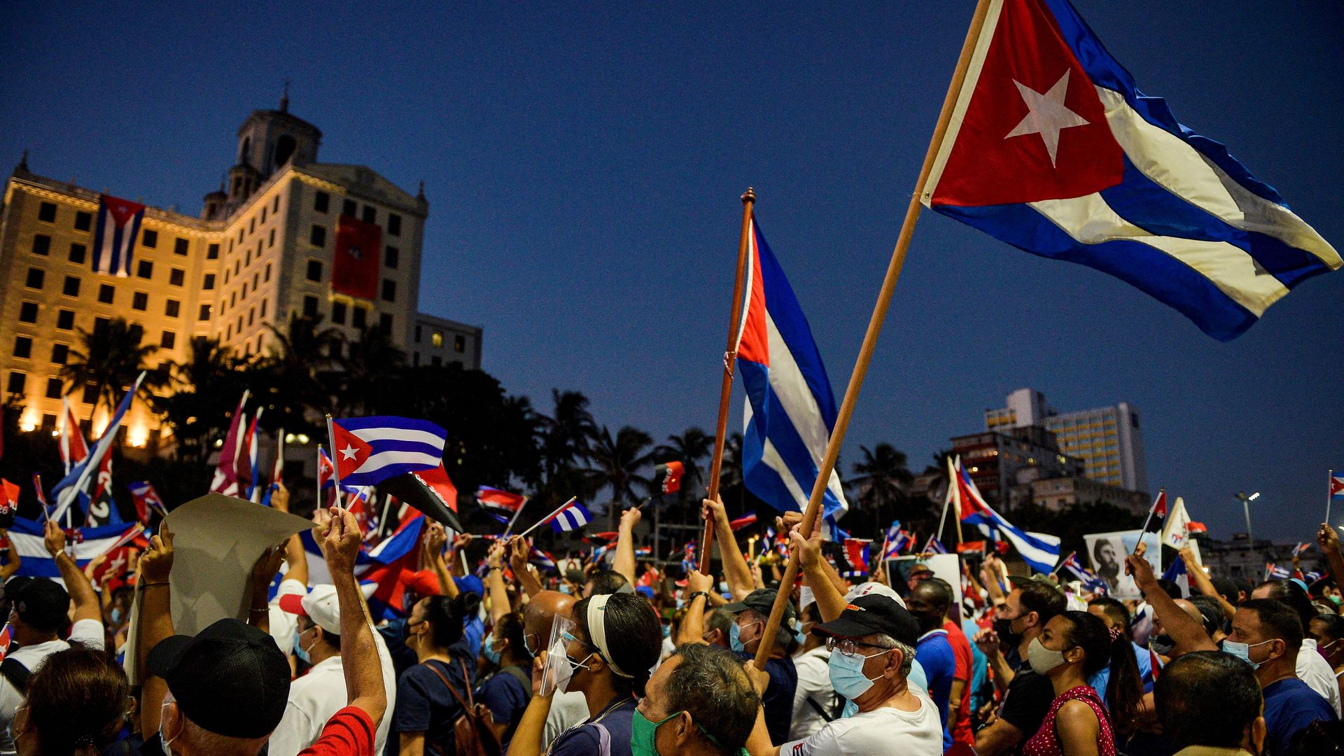 Picture of a protest in Cuba with a crowd of people, they're all wearing masks and holding Cuban flags