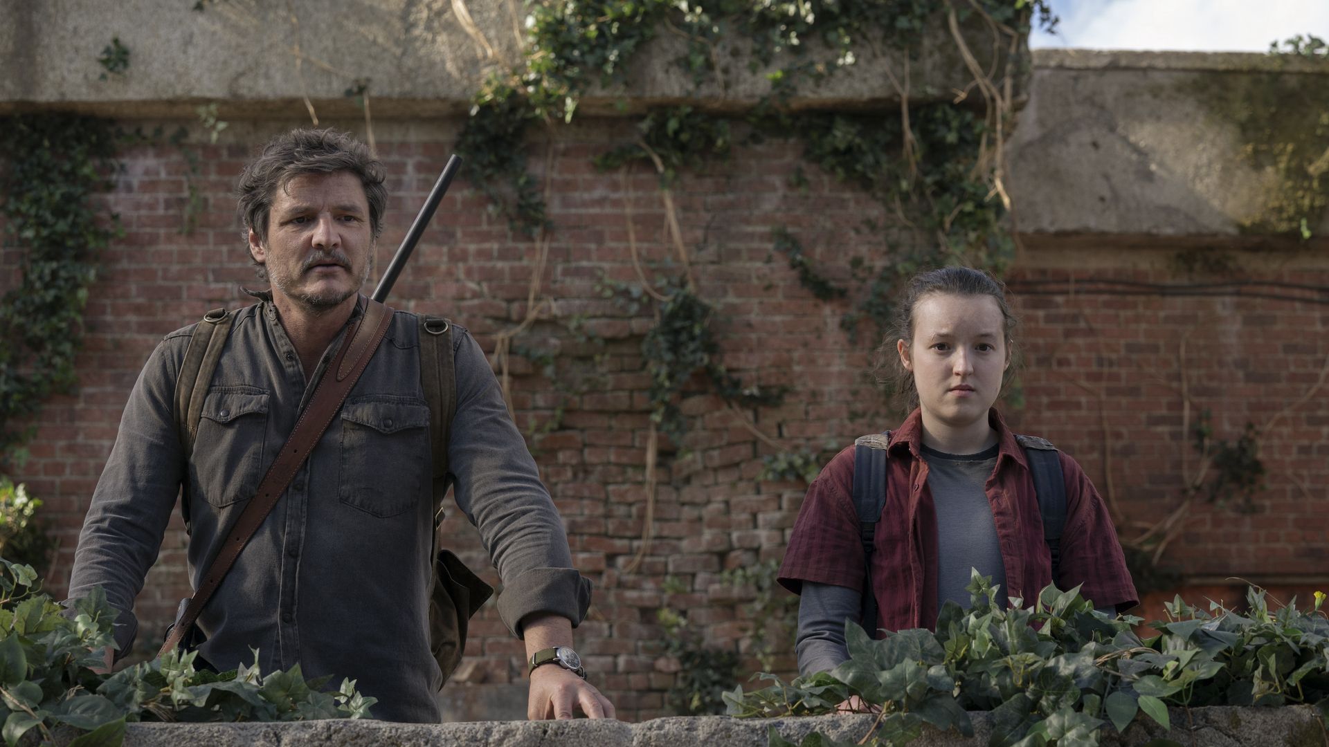 Video still from The Last Of Us TV series showing two actors standing in front of a brick wall
