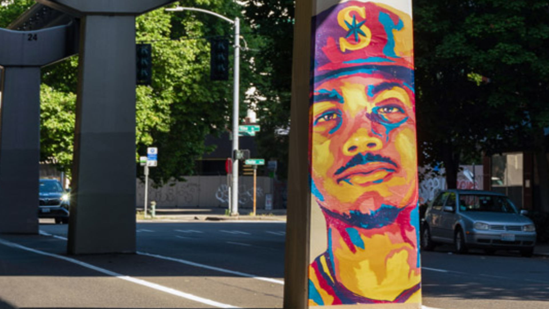 A colorful mural of Mariners player Julio Rodriguez is shown on a pillar of the Seattle Monorail with Fifth Avenue surrounding it. 