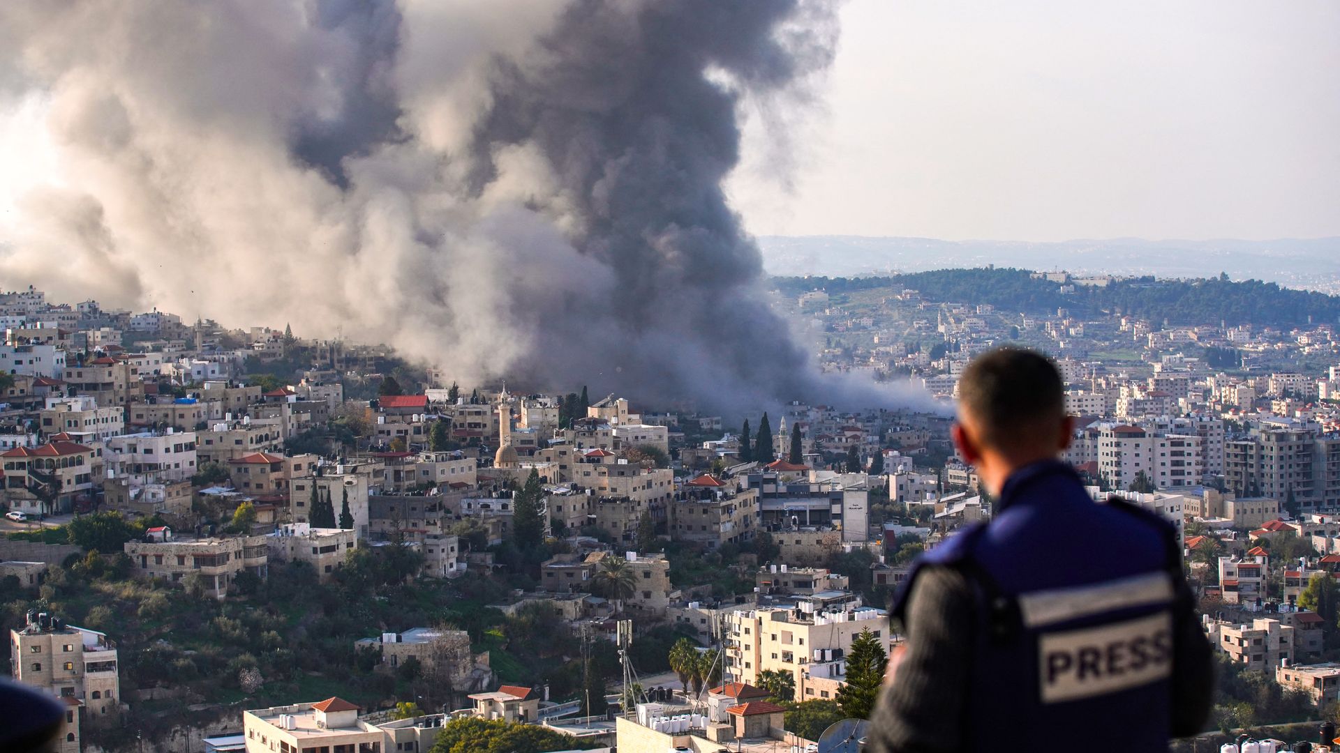 A journalist looks on as smoke billows from the site of several explosions during an Israeli raid on the Jenin camp for Palestinian refugees on Feb. 2, 2025. 