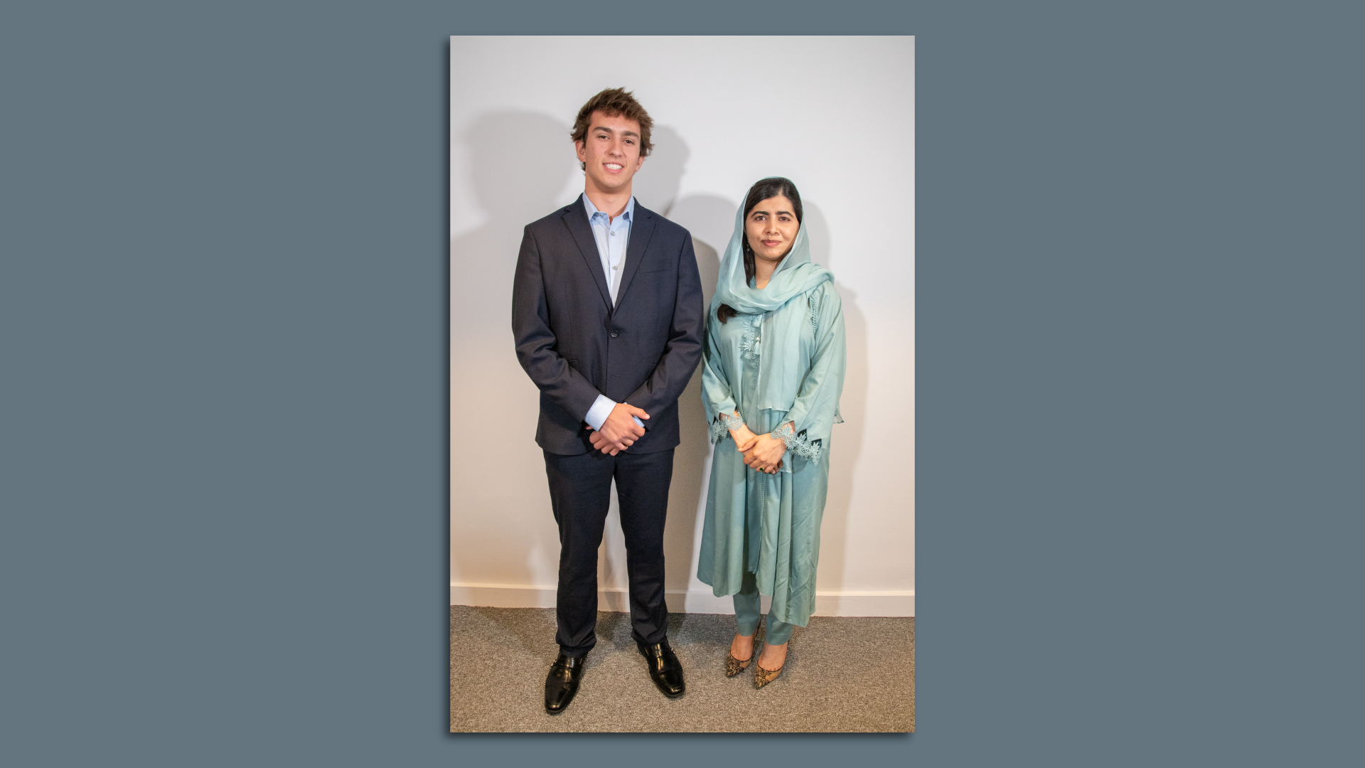 Theo Valles stands in a grey suit next to Malala Yousafzai, in a pale blue dress and headscarf. 