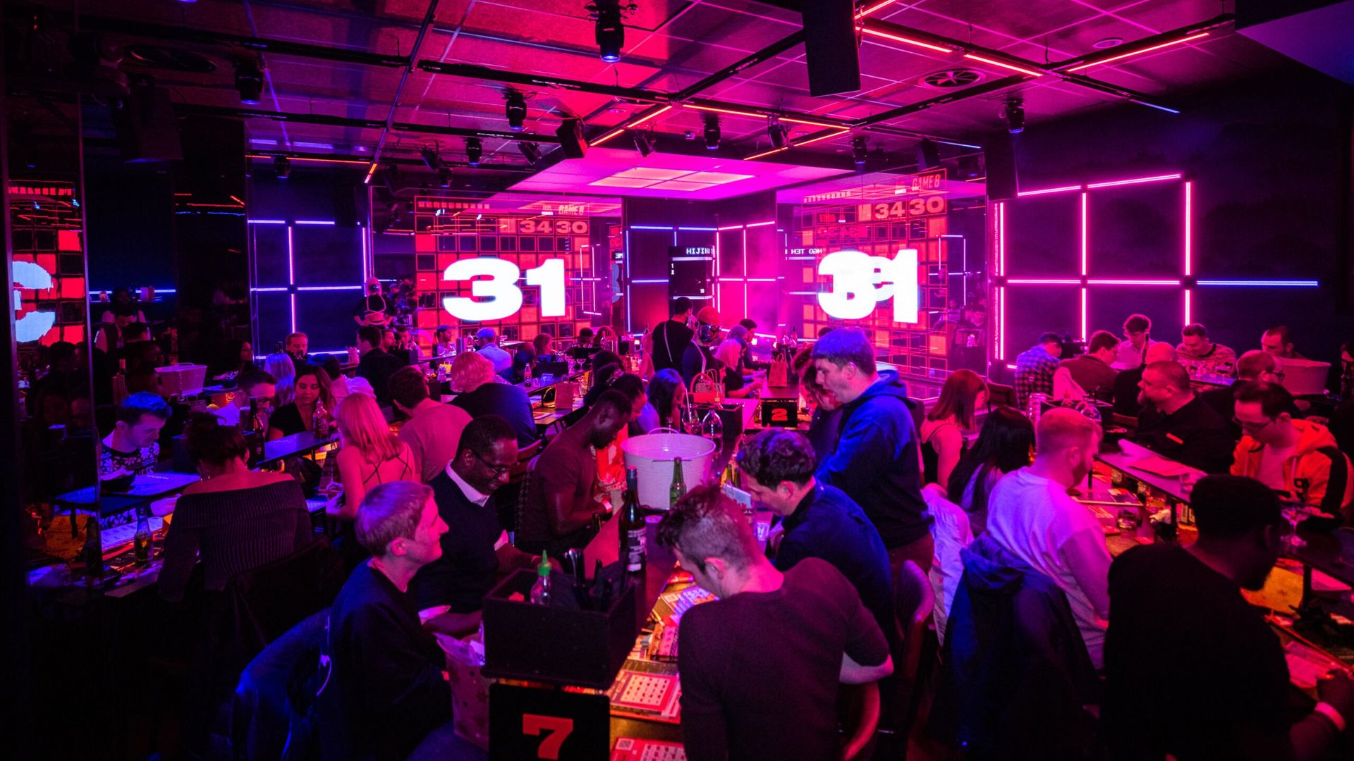 A nightclub interior where people are playing bingo and the number "31" is flashed in giant screens.