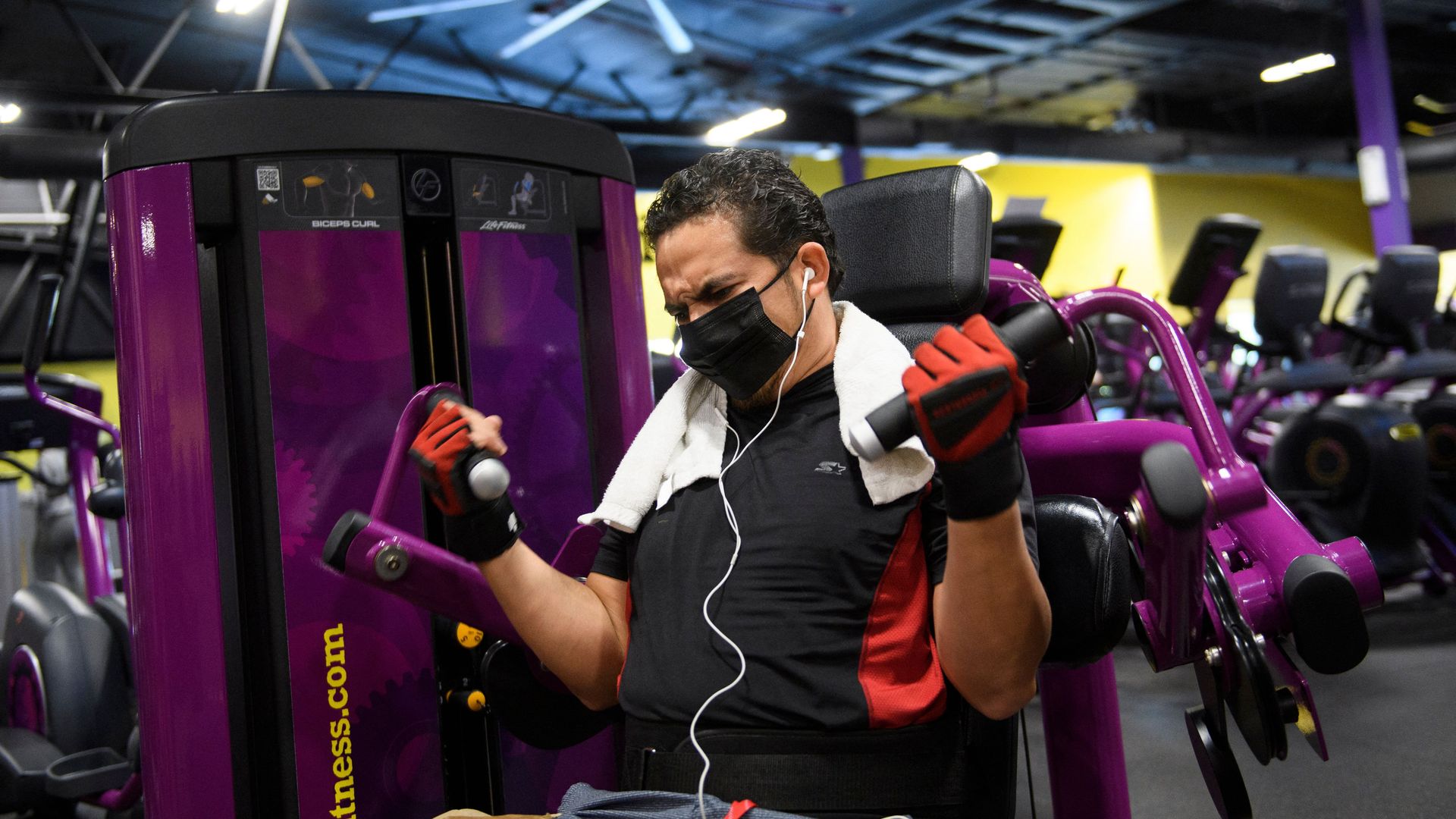 Man wears a face mask while using a weight machine inside a Planet Fitness gym.