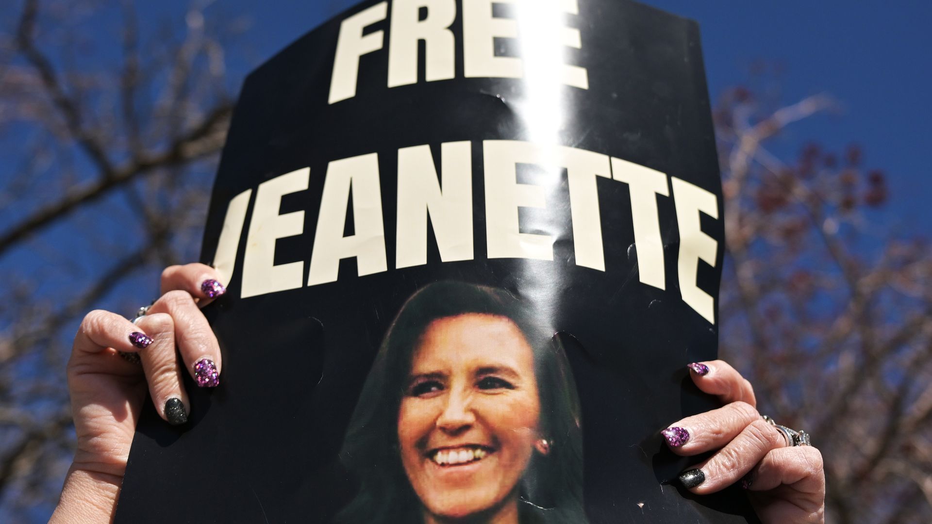 A woman holds up a sign reading FREE JEANNETTE.