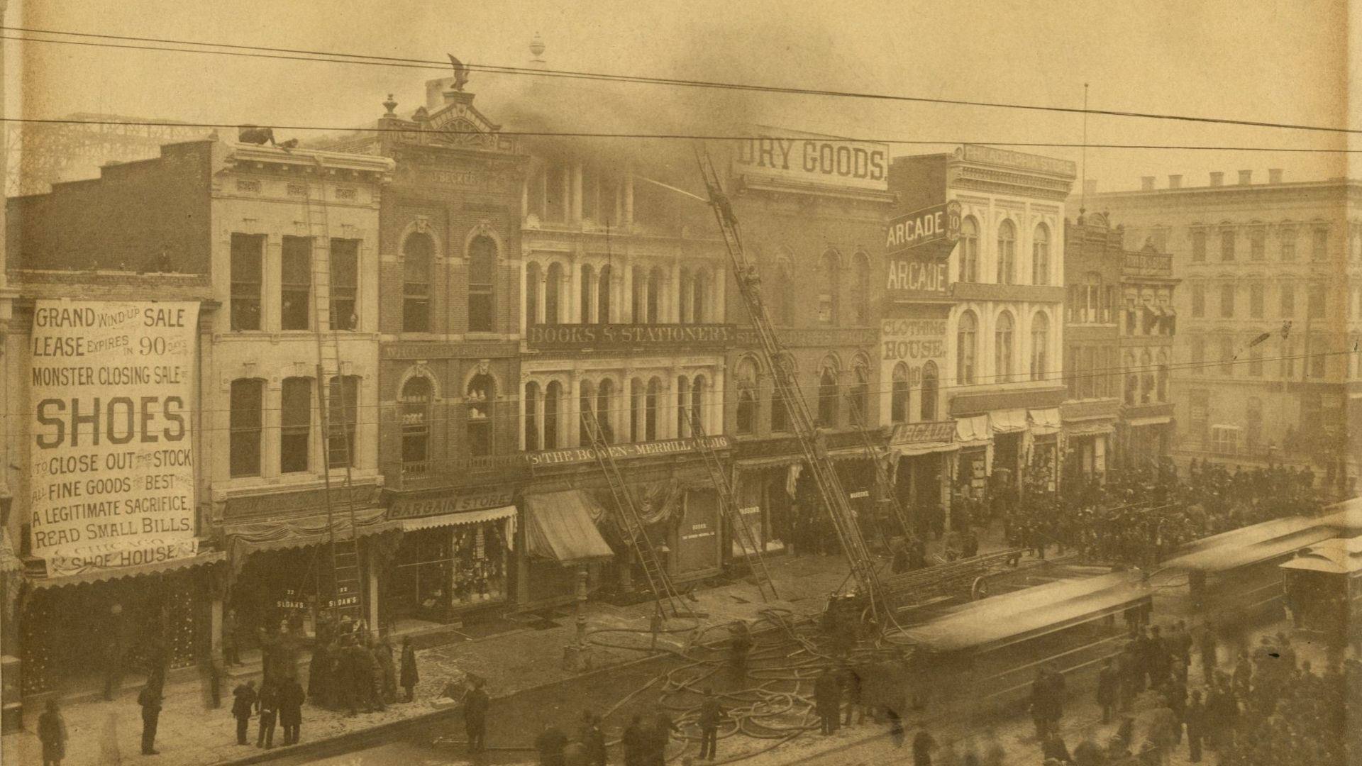 Sepia-toned 19th-century street with a row of arched storefronts, signs reading DRY GOODS and ARCADE, a large shoe-sale banner, and a dense crowd along the curb beneath overhead wires.