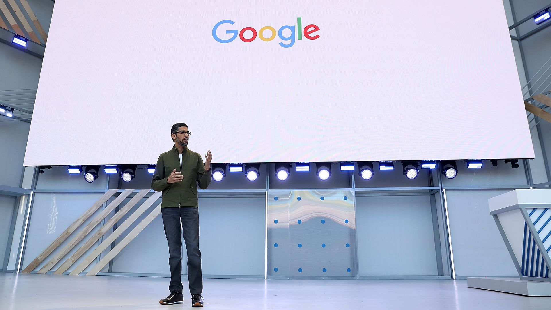 Google logo on a white screen above Sundar Pichai talking with hands up