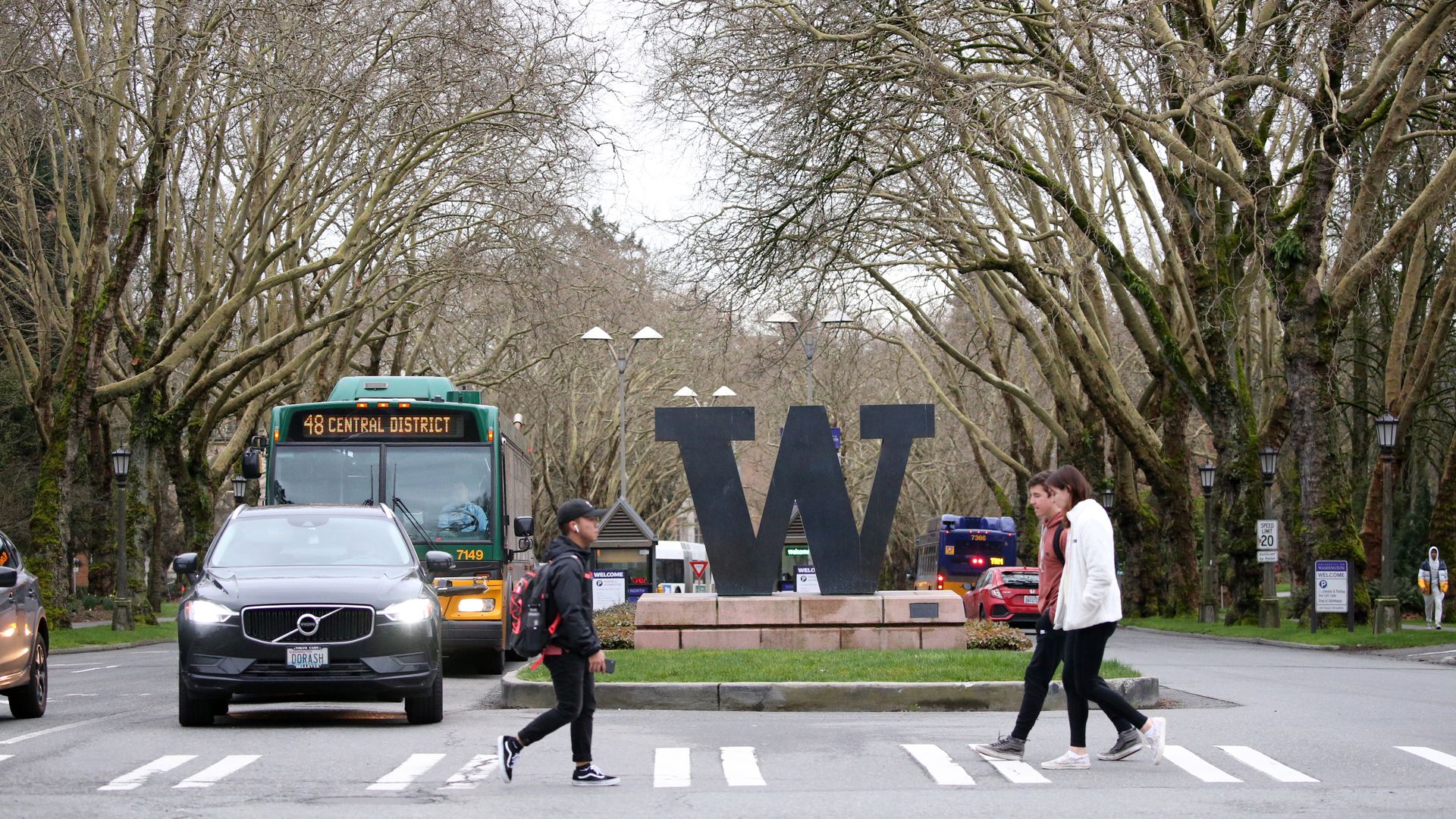 Students cross a street with cars and a large "W" in the background. 